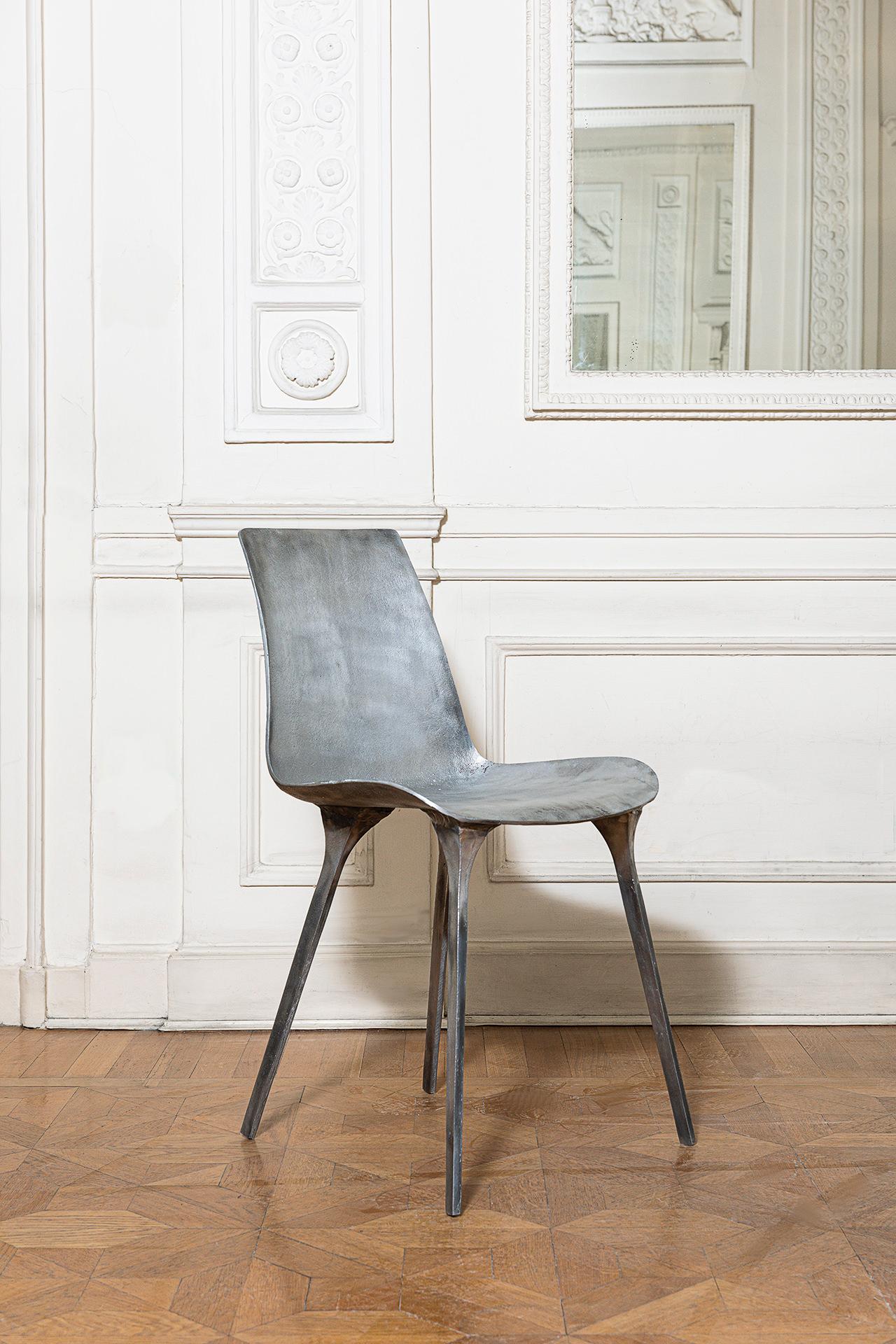 The solid metal Sylvie chair is made entirely of cast aluminum silver, left in its unfinished state. The body is formed of a shell-like seat with a rounded backrest and four tapered legs. The textured surface of the solid metal chair makes it seem