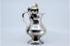 Silver milk jug w/ simple handle, lid w/ knob & resting on a base w/ frieze