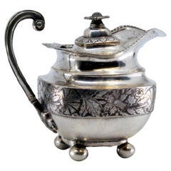 Silver milk jug with chiseled florals, missing handle, and knobbed lid