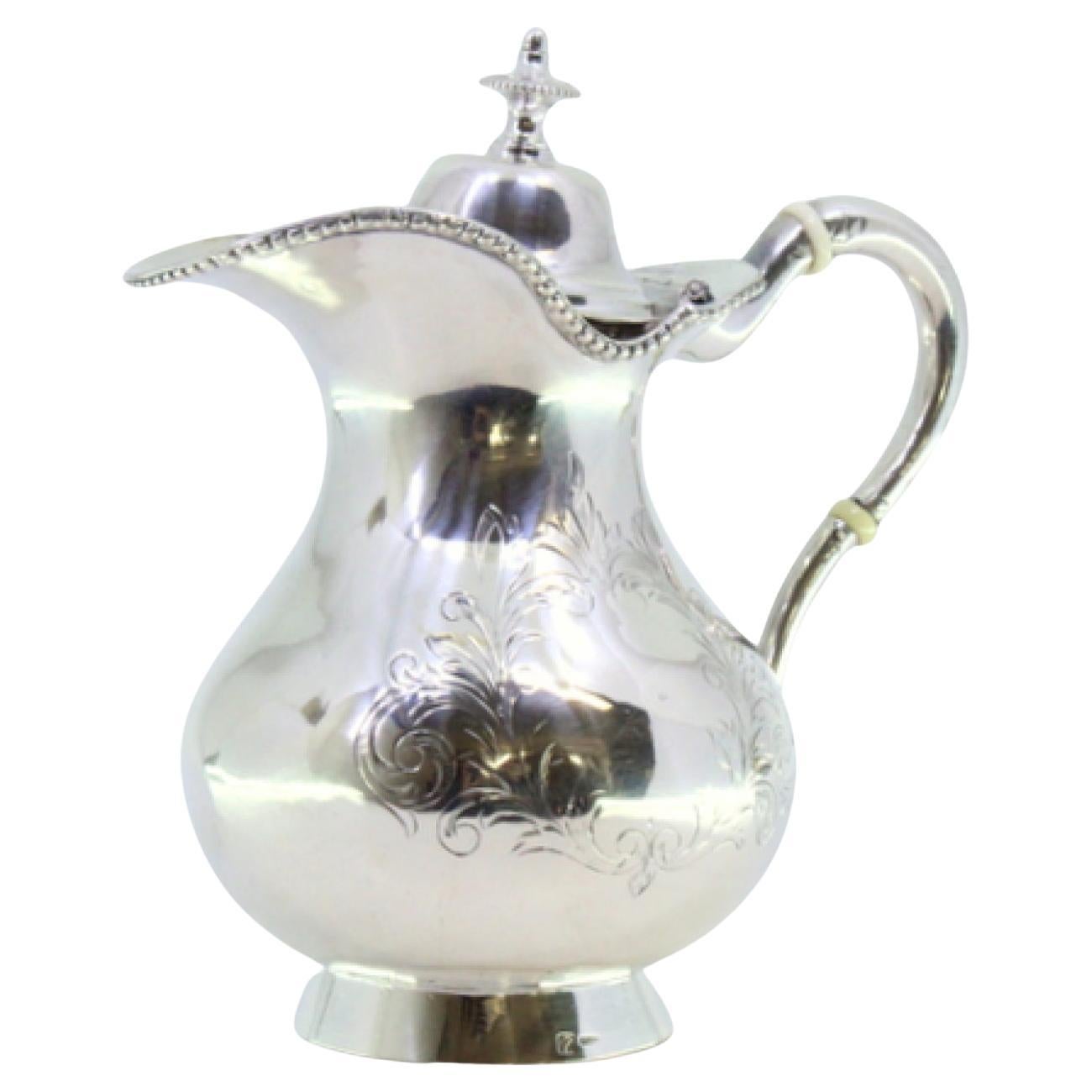 Silver milk jug with plant engravings, monogram card, and knobbed lid