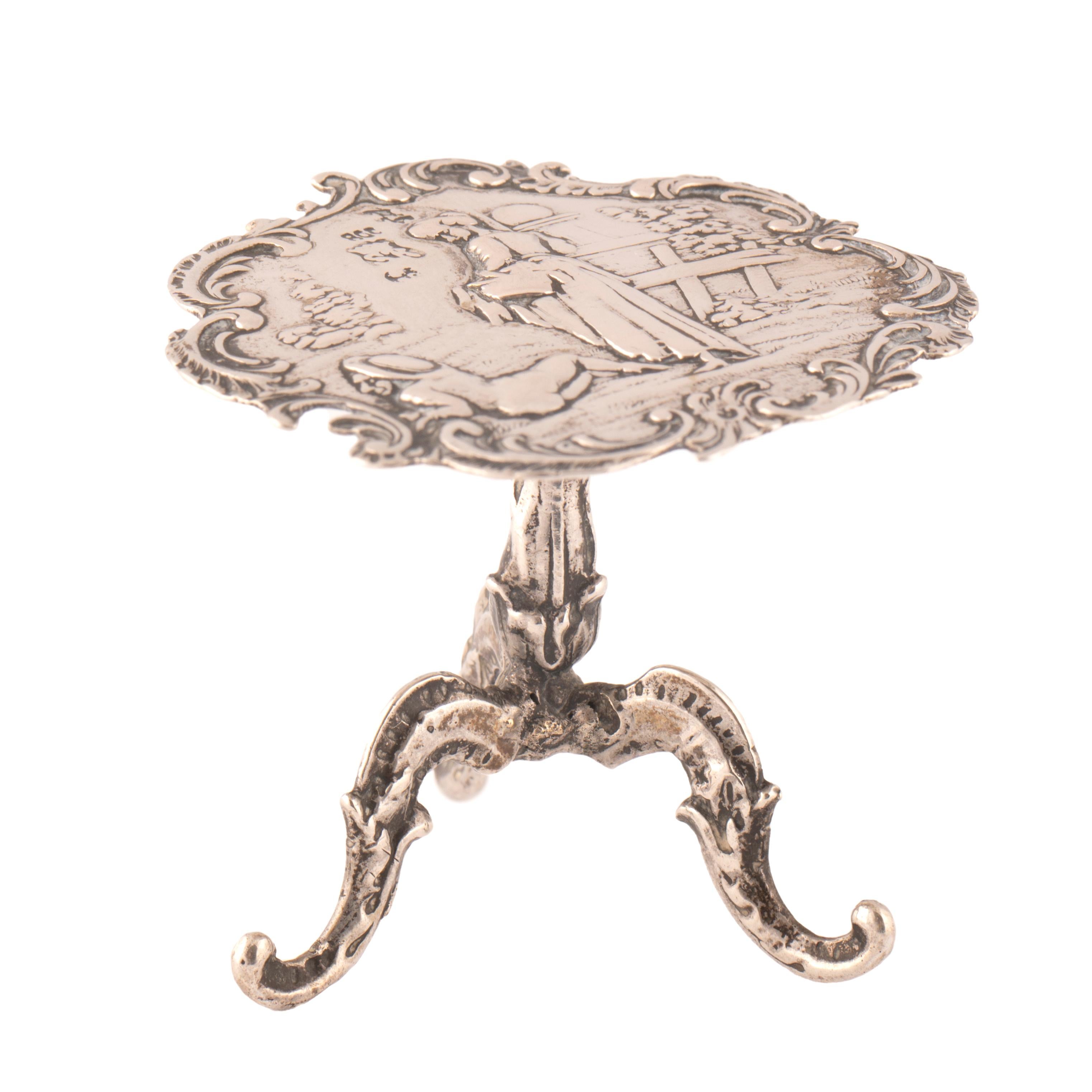 Charming miniature silver Rococo style pedestal table made at the turn of the last century for a doll house.  In the Romantic taste, the shaped circular tabletop of repoussé silver recalling paintings by the French 17th century artist Watteau