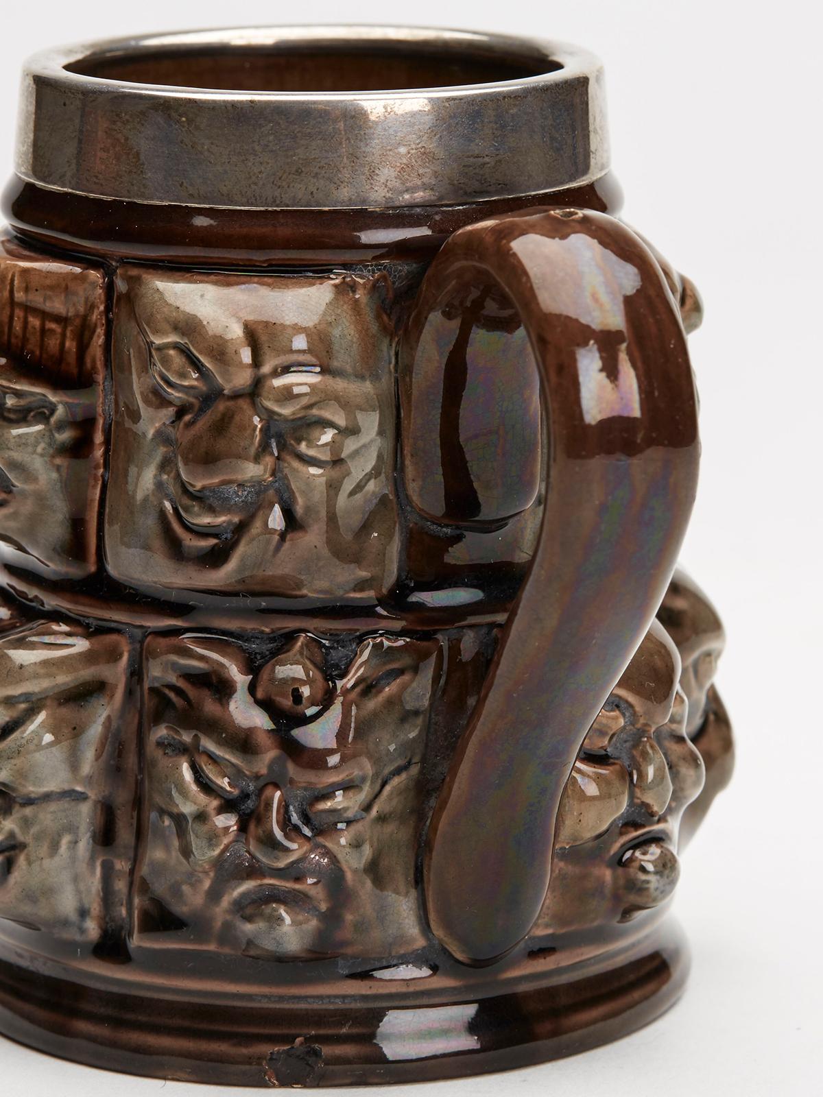 A very unusual Aesthetic Movement art pottery silver mounted mug modeled in relief with thirteen grotesque faces and dating from around 1880. The finely potted mug is heavily relief molded with thirteen square panels each modeled as a grotesque