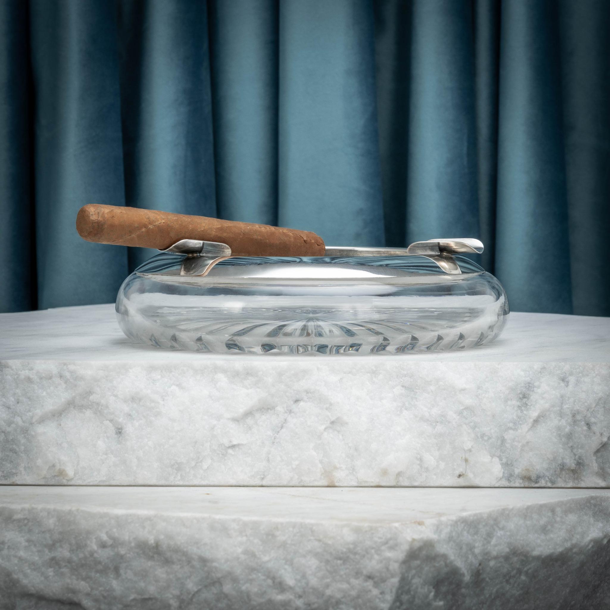 A splendid glass and silver cigar ashtray with cut glass base and three silver rests for cigars; circa 1935. Has silver marks of the Imperial crown and crescent moon for Germany, a silver purity stamp of 925 (same purity as sterling) and makers