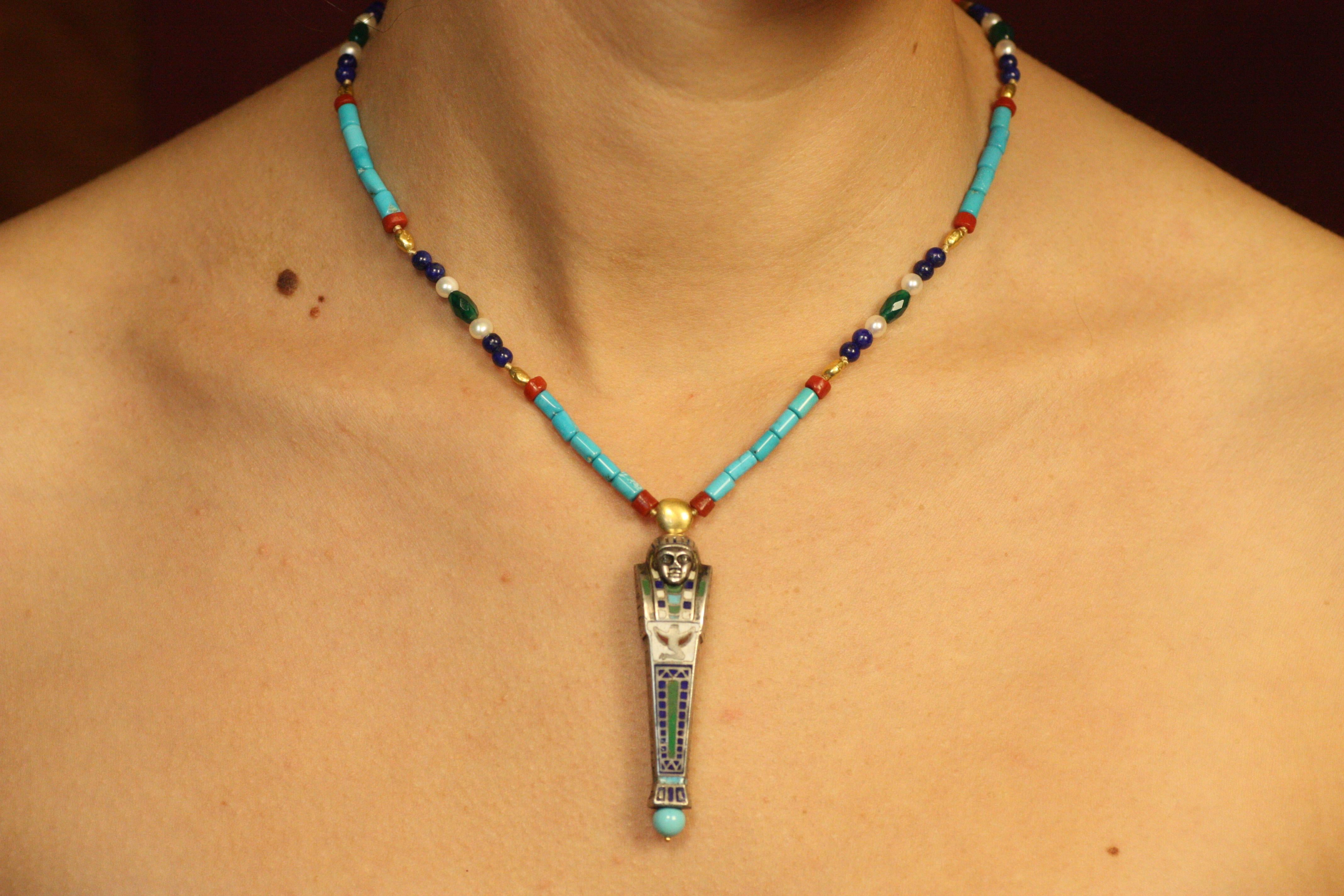 This one-of-a-kind Mummy Beaded Necklace tells a story of discovery and reinvention. The mummy centerpiece is a “found object” repurposed from a 1920s mechanical pencil that was part of an Egyptian Revival desk set. Its hand-enameled details on