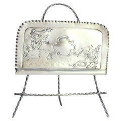 Silver napkin holder with engraved maritime motifs and set on three feet