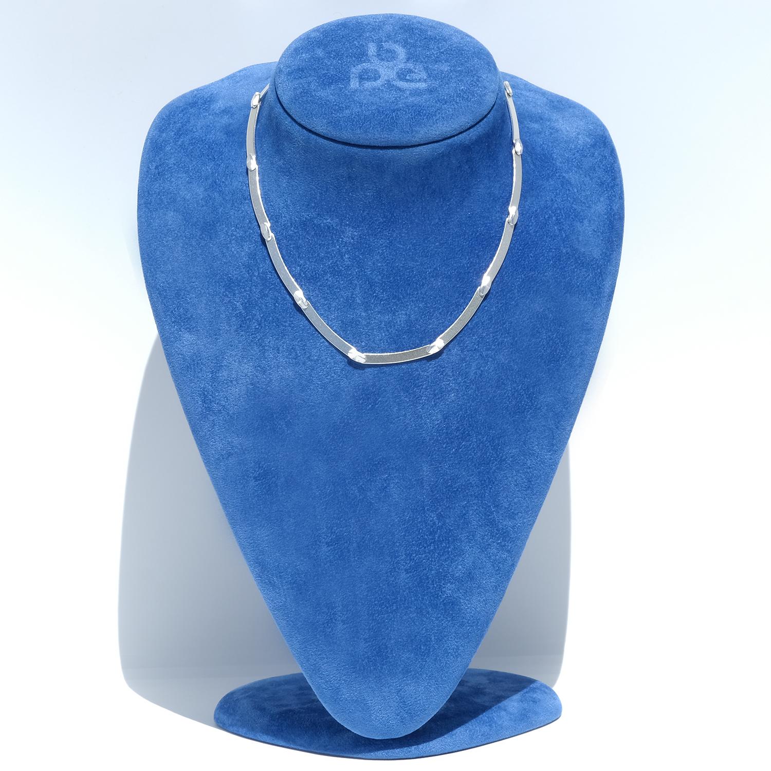 Diese Halskette aus Sterlingsilber besteht aus leicht gebogenen, flachen Gliedern, die durch kleine dekorative Silberringe zwischen den einzelnen Gliedern verbunden sind. Es hat eine klare, dezent matte Silberoberfläche, die dem Design einen