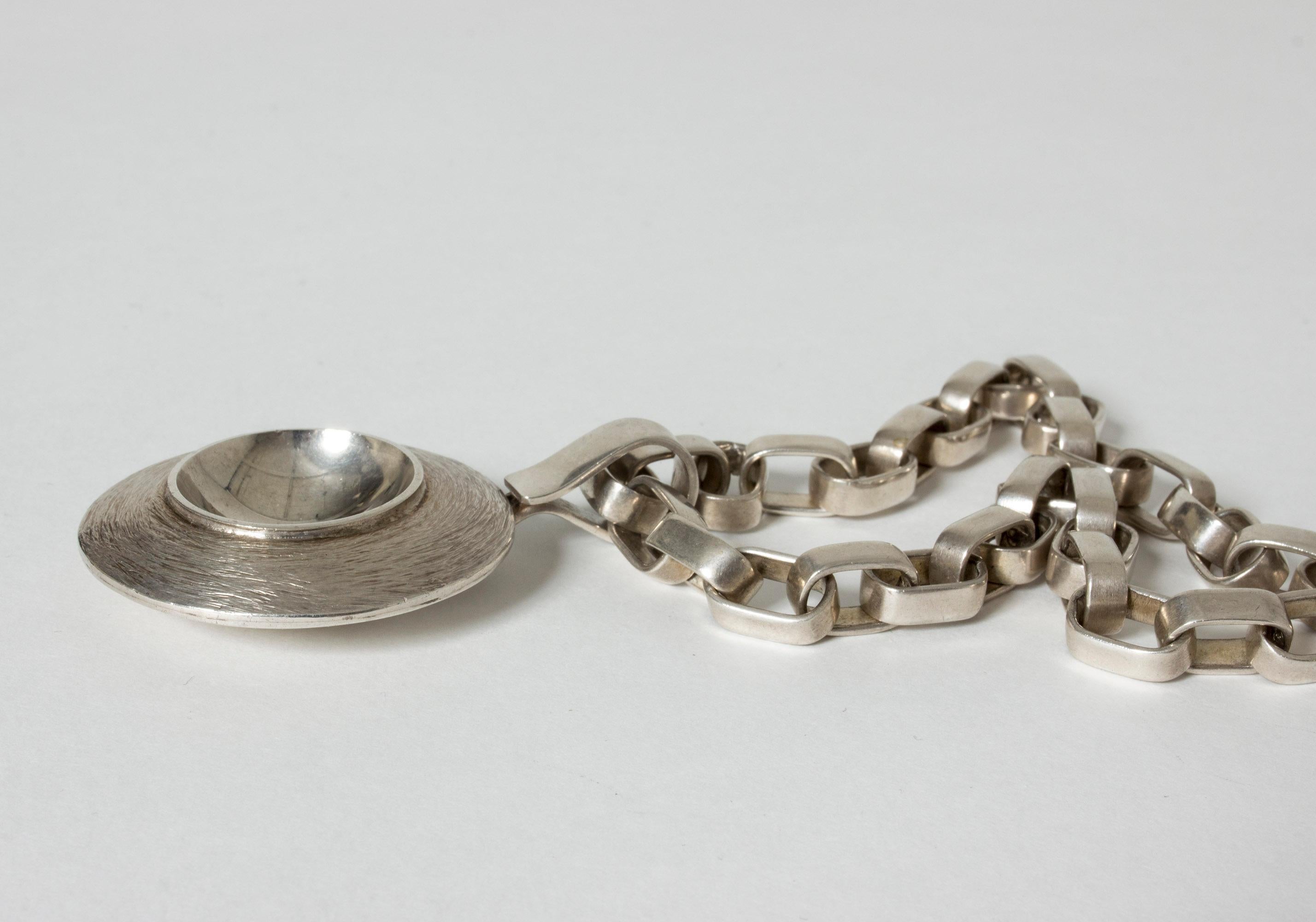Magnificent silver necklace by Sven-Erik Högberg with a hypnotizing, round pendant on a thick chain that can be worn just as well on its own. Wonderful design and craftsmanship.

Year: 1974 (pendant) and 1978 (chain)
Dimensions: Height 6.5 cm