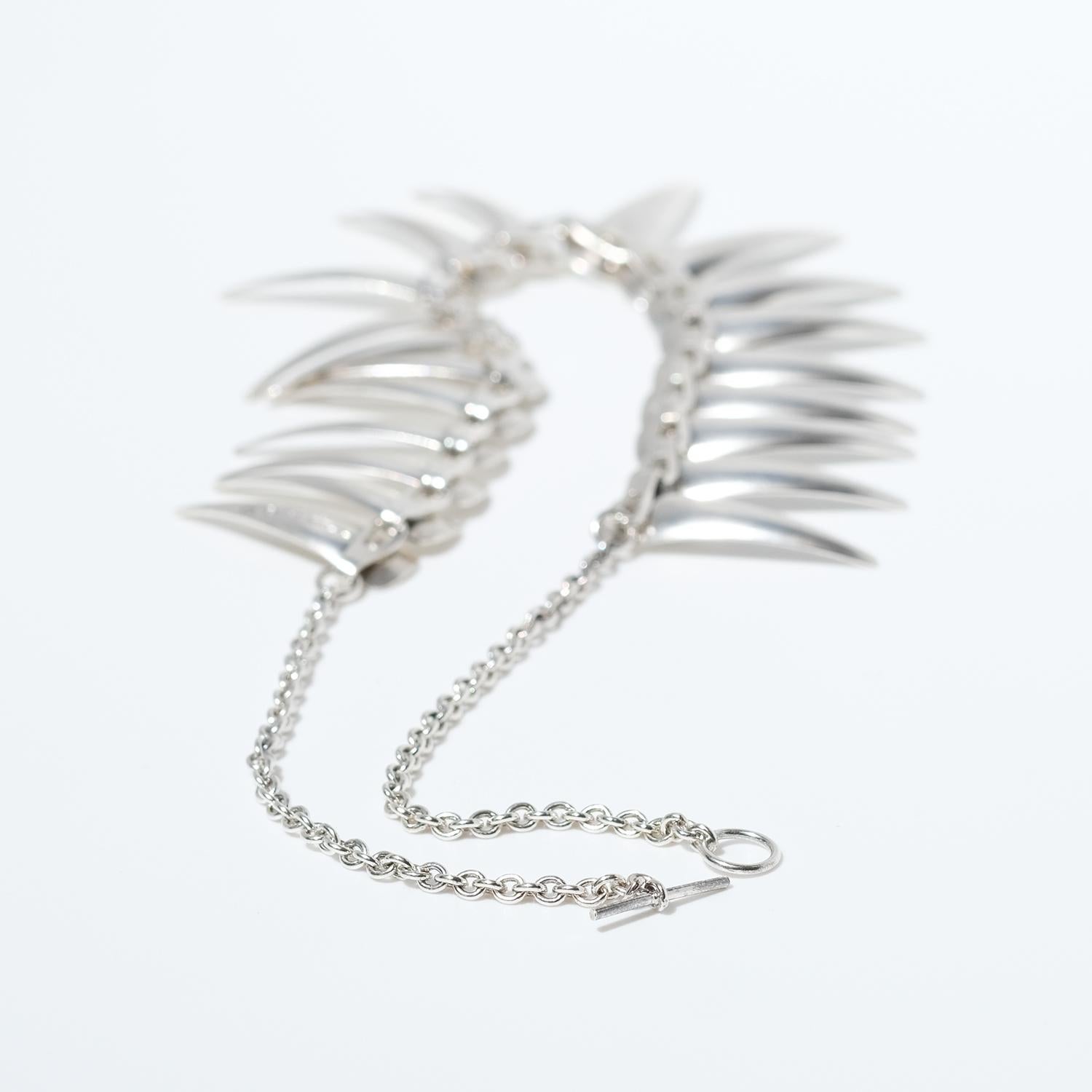 This sterling silver necklace is adorned with 20 slightly brushed silver pendants shaped as shark teeth. It closes easily with a circle and a bar. The necklace is a so called choker, meaning a necklace with a very close fitting around the neck.

The