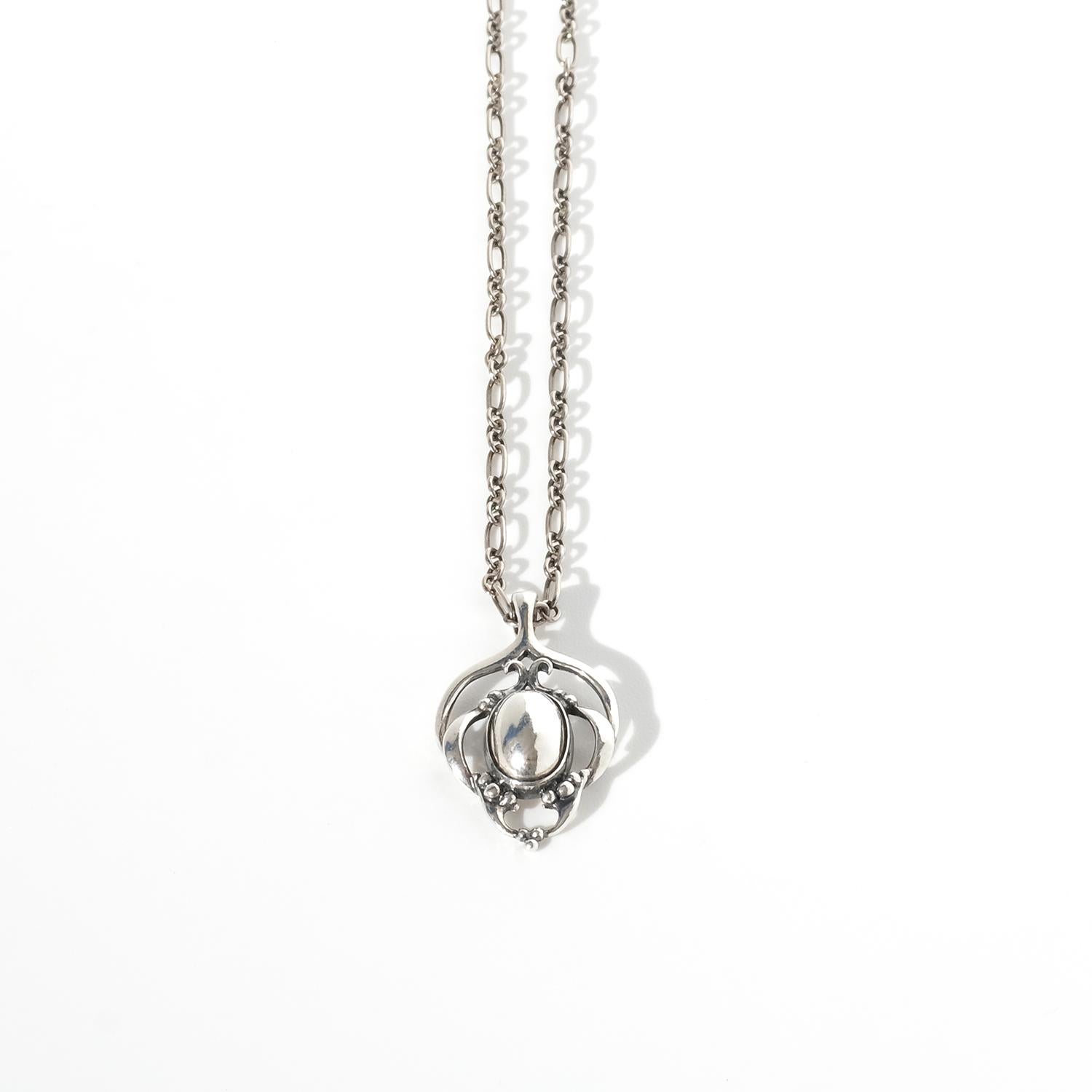 This vintage necklace / pendant from Georg Jensen's Heritage collection is a timeless piece in sterling silver, inspired by Art Nouveau aesthetics. The pendant showcases an oval-shaped polished silver centerpiece, encased in flowing, organic silver