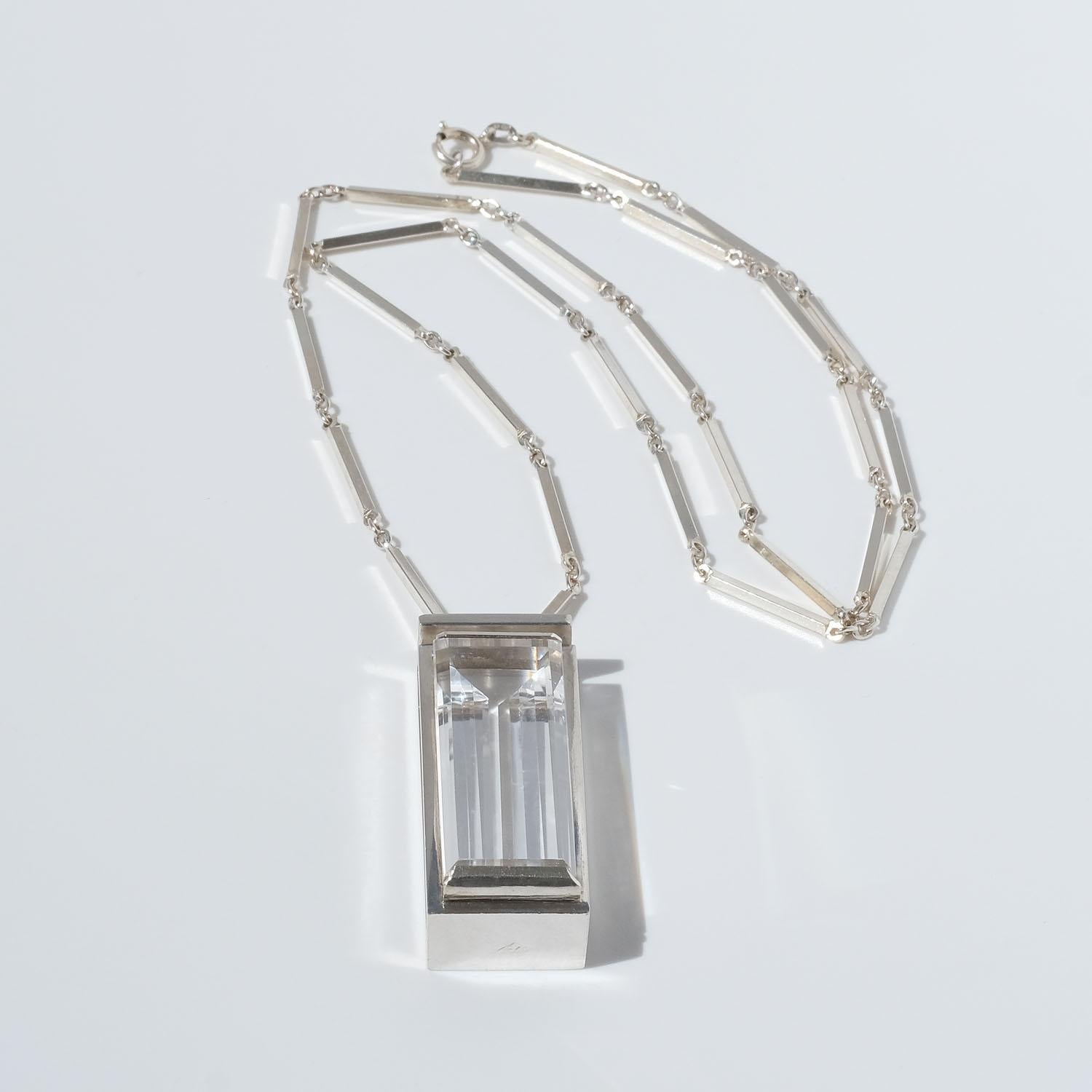 This silver and rock crystal necklace shows upon typical Art Deco style characteristics, such as the ring and bar chain, the pendant with its straight geometric shapes, its shiny surface and the baguette-cut rock crystal.

This elegant necklace fits