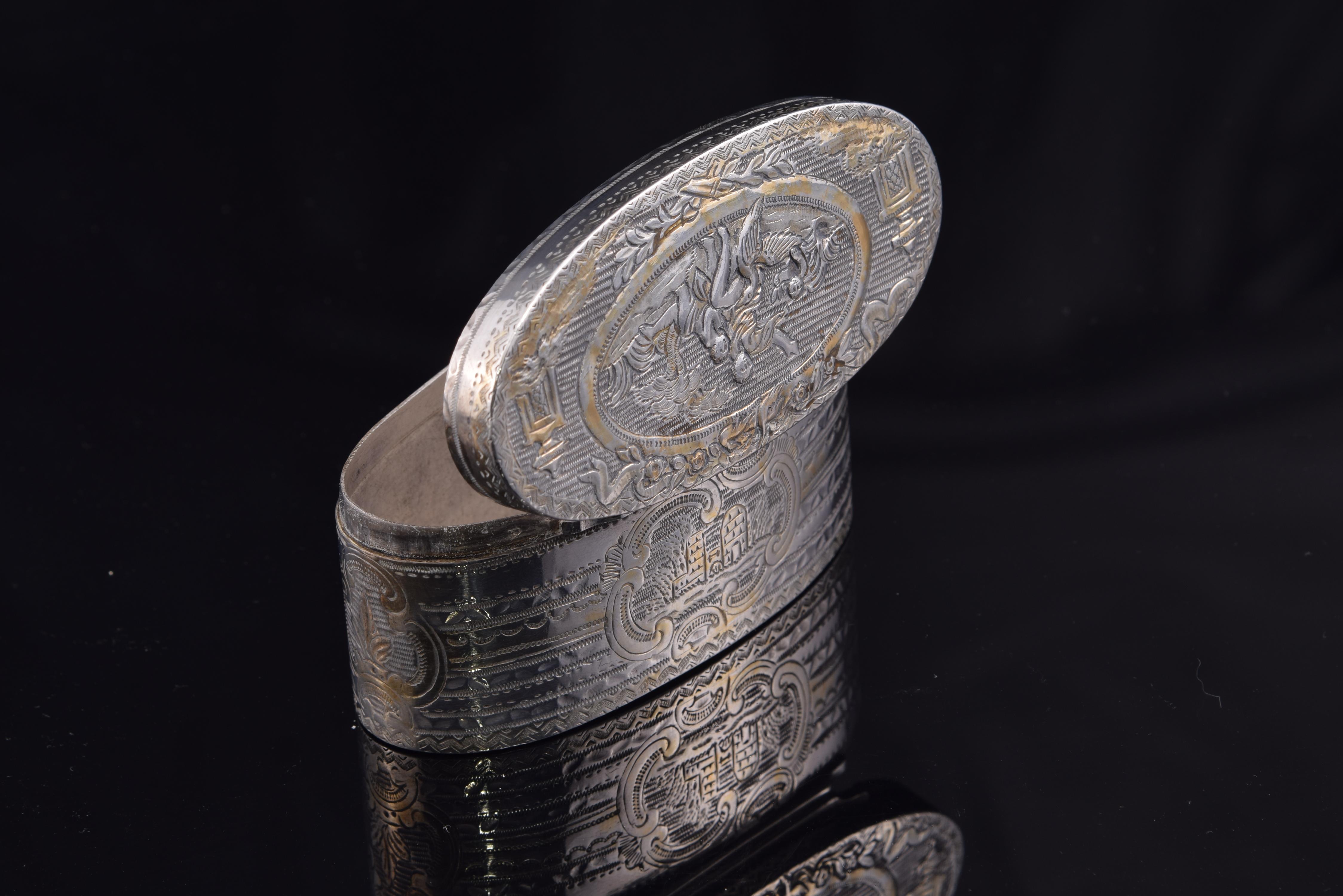 Oval box. Silver, 19th centu.
 With contrast marks.
 Oval box with flat lid made of silver, partially gilded, decorated on the outside with figurative scenes and framed landscapes and geometric motifs arranged in a band, architectural and plant. The