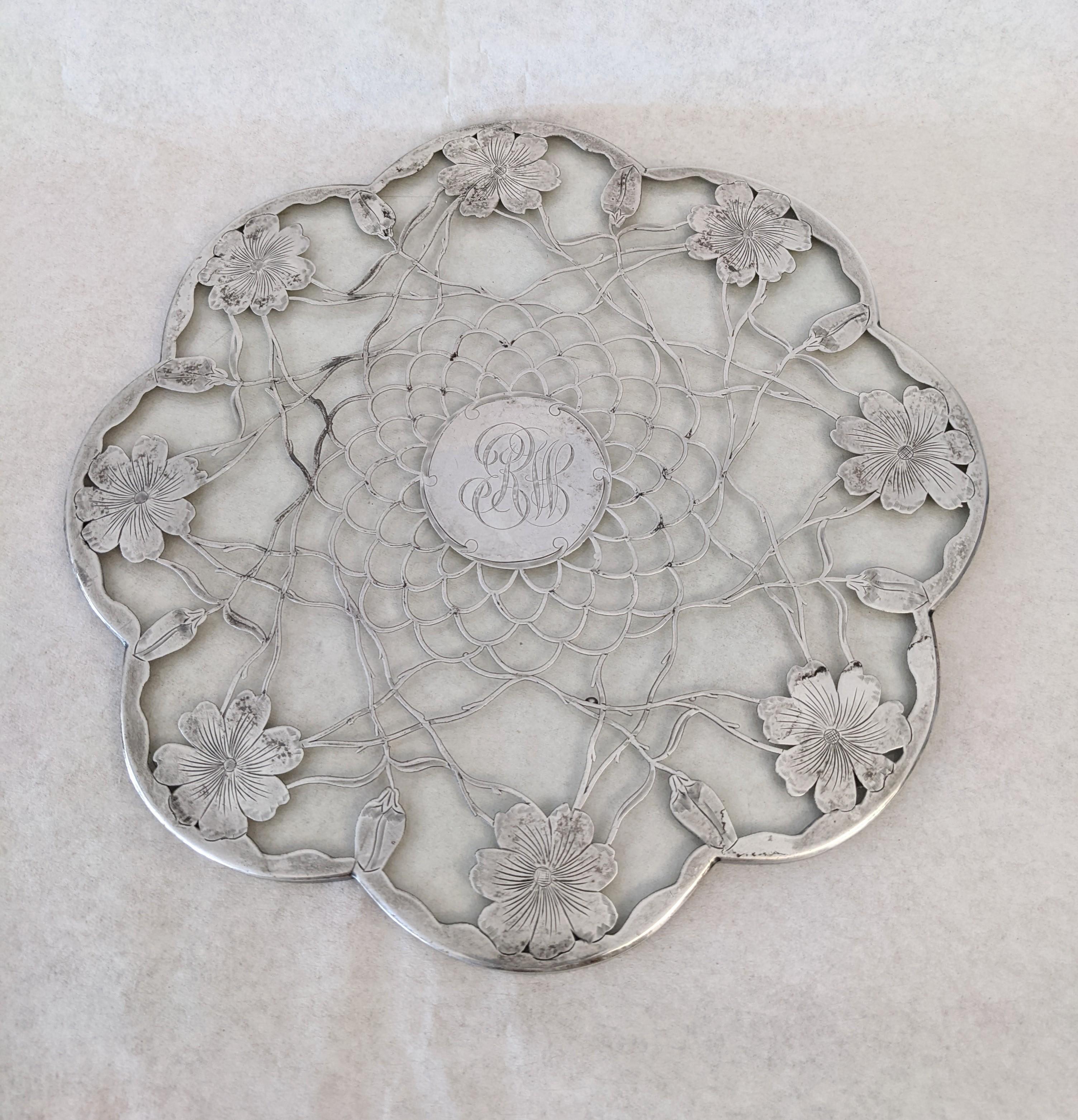 Sterling over glass trivet from the Art Nouveau period. Thick sterling floral and vine patterns are used to form the overall design. Sterling makers mark on side. The glass is scalloped on the edges. 
10