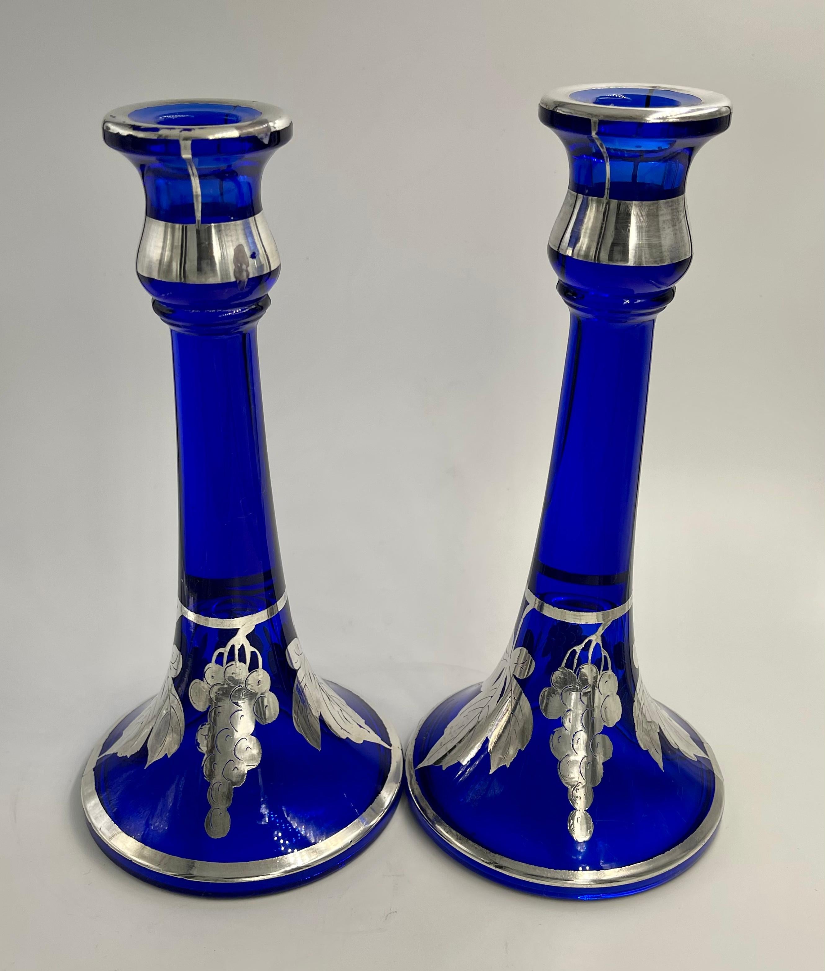 Pair of cobalt blue candlesticks with flash silver overlay ( the thinner version of silver overlay). Gorgeous blue candle holders with 4 lines going from rim to bottom. The bottom flares and is decorated with 2 vines of grapes and 2 leaves on each.