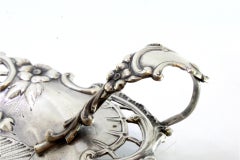 Silver paddle with floral motifs in relief and set on three flower-shaped feet