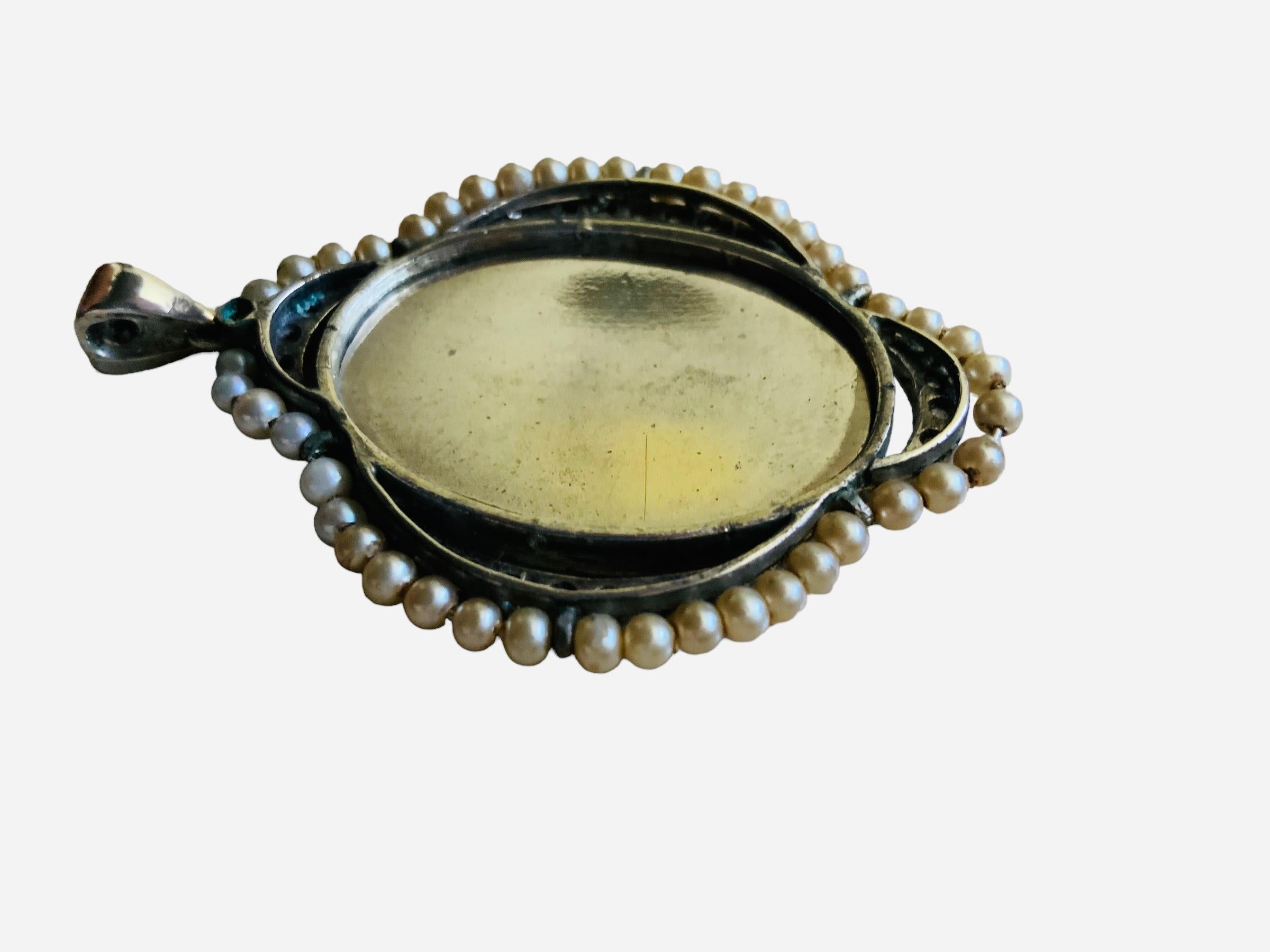 Il s'agit d'un pendentif religieux en argent avec des perles et des pierres claires. Il représente un boîtier ovale en verre argenté avec un portrait peint à la main de la Vierge Marie priant les mains jointes. L'extérieur du boîtier est orné d'une