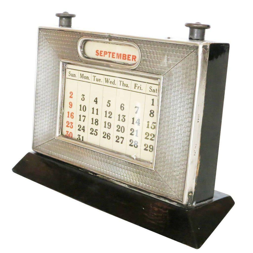 This piece is a silver frame perpetual calendar atop an ebonized wood frame with changeable calendar under glass. On the back of the frame is an accessible wooden door that enables the owner to change calendar months. It comes with all the cards
