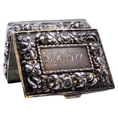 Silver pill box decorated with flower reliefs on the hinged lid