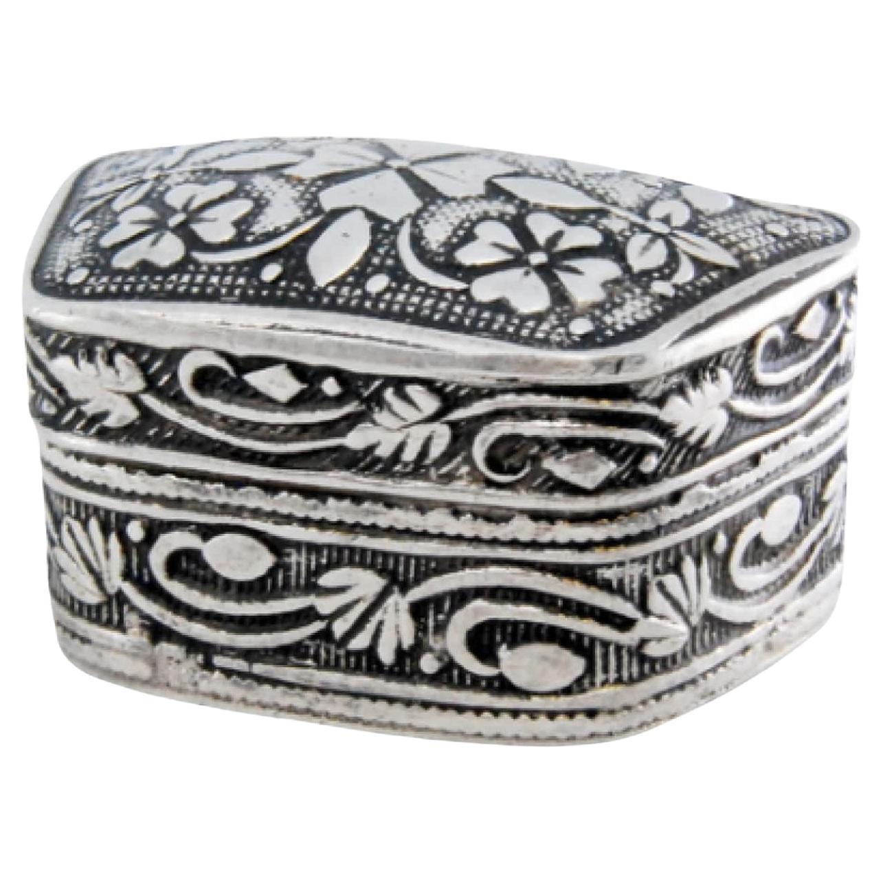 Silver pill box with raised plant motifs on the casing and removable lid
