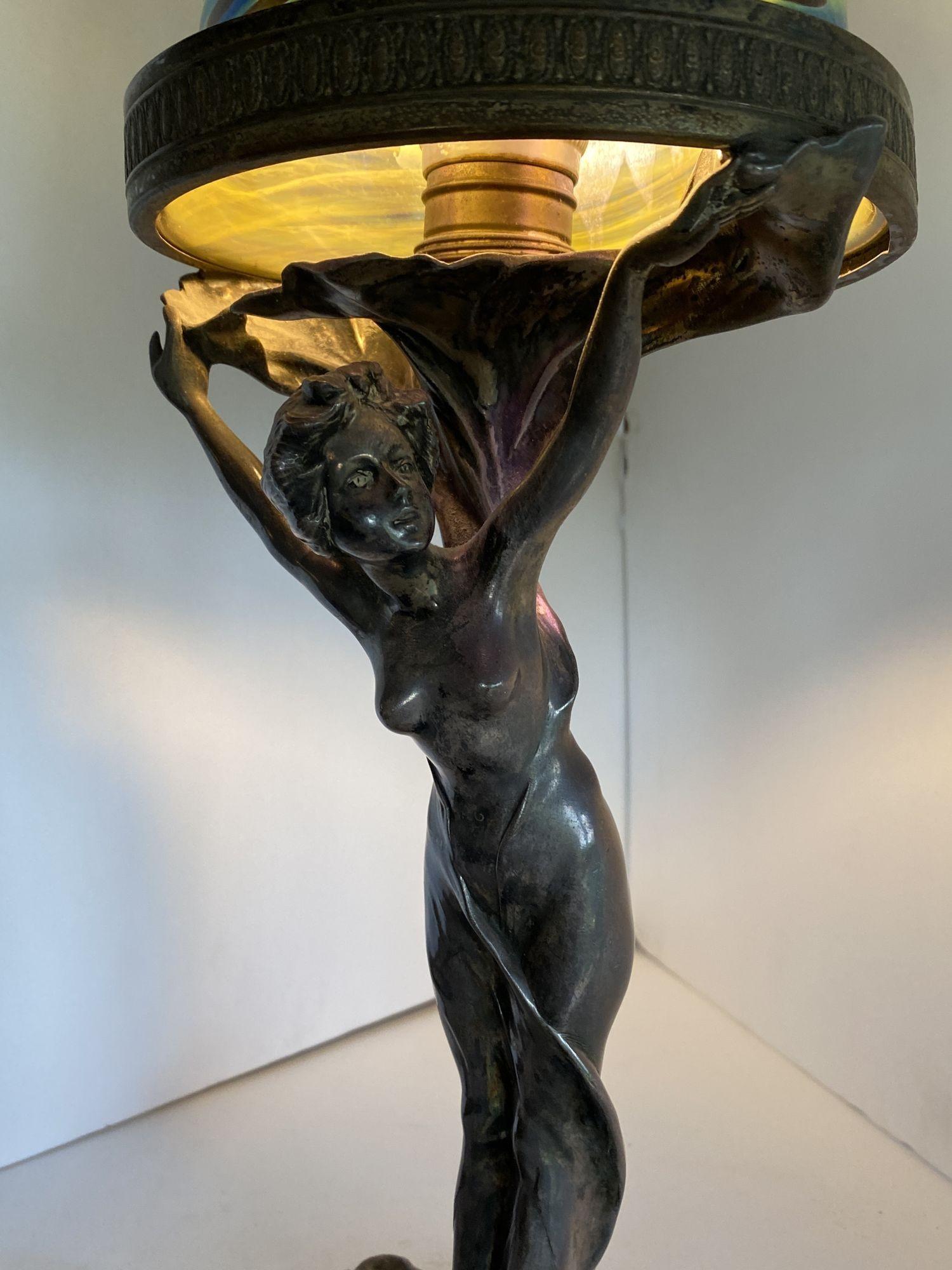 Silver plate bronze Nude female Art Nouveau lamp featuring a young nymph holding up a large Iridescent Art Glass Shade. The lamp features an organic form and has been rewired with an original brass acorn light switch. 
 
Circa 1900.