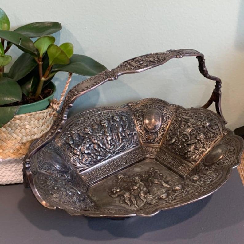 Questo splendido cesto antico di epoca vittoriana placcato in argento è uno squisito esempio dell'artigianato della fine del XIX secolo. Il cestino presenta intricati dettagli repousse, con delicati cherubini e grappoli d'uva, un segno distintivo