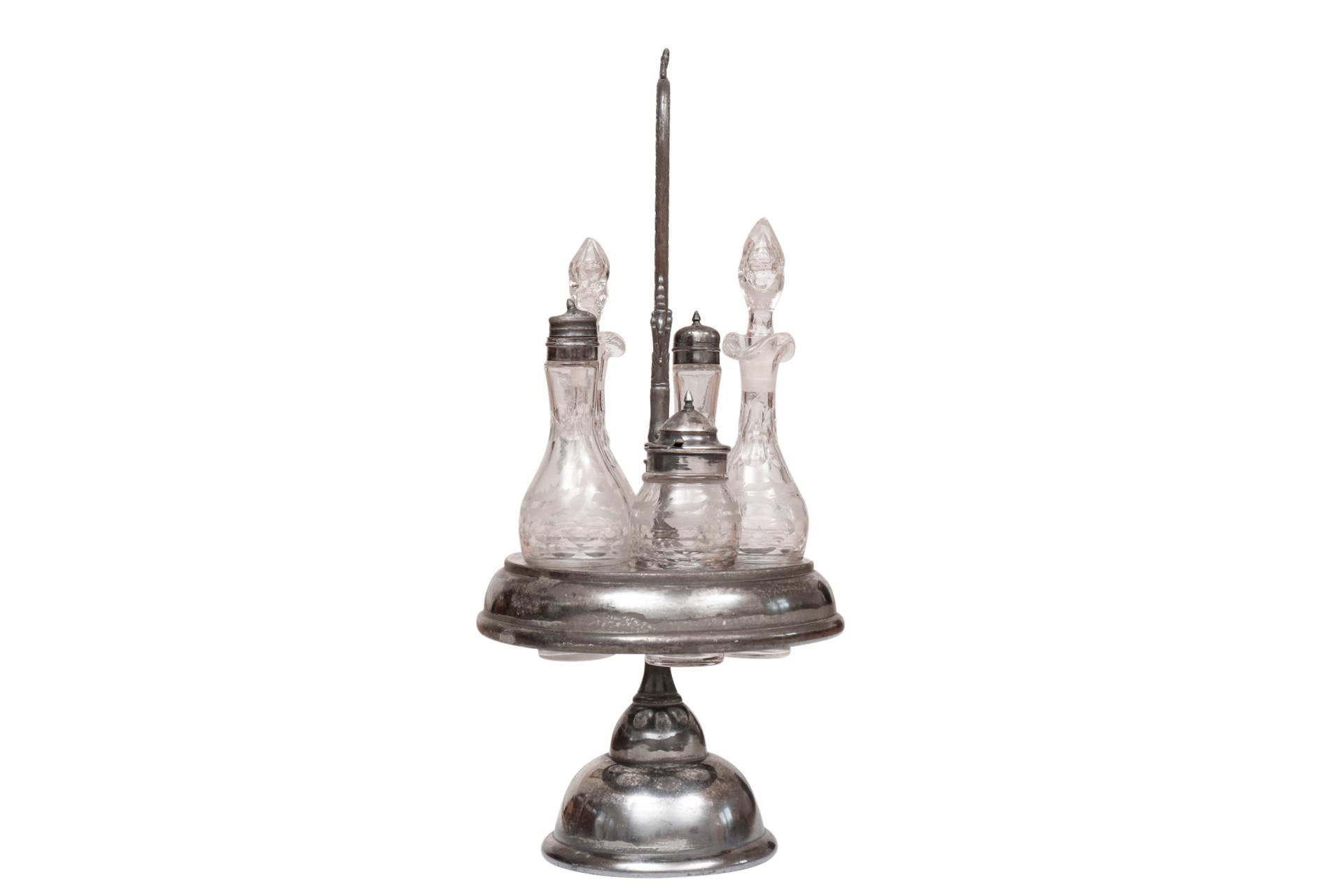A silver plated cruet condiment set. Five etched glass bottles serve to hold salt, pepper, oil, vinegar and soy sauce. The caddy rotates and a single handle is ornately pressed with reeded lines and a simple floral motif.