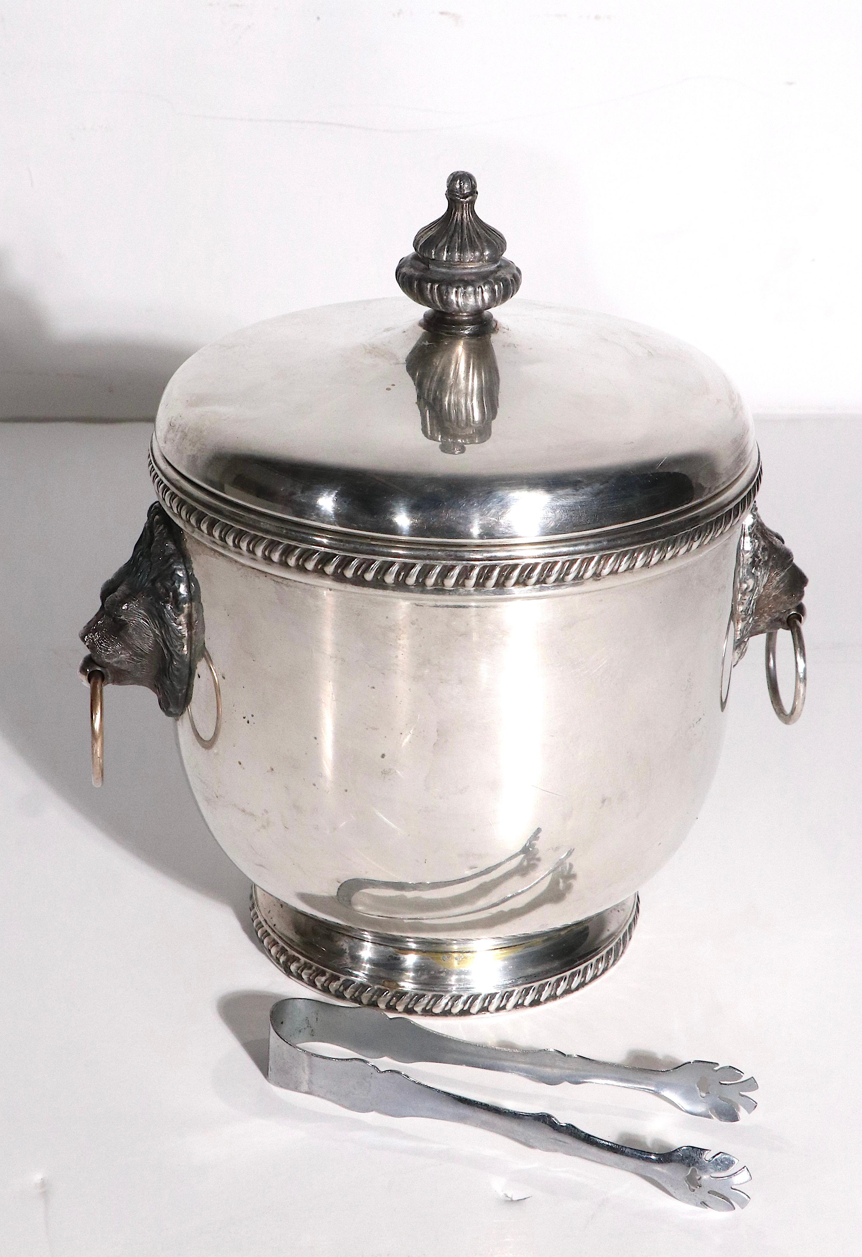 Silver plate ice bucket by The Sheffield Silver Company. The ice bucket features lions head appliqués with ring handles, and  original white milk glass liner. This example is in  good original condition, showing some cosmetic wear and minor dents,