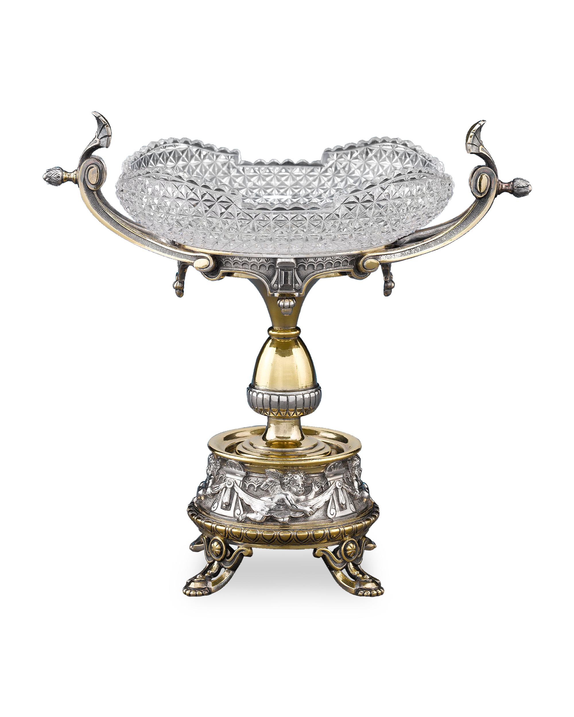 This stunning pair of silver plate tazzas by Elkington and Co. exhibits a classical elegance. Greco-Roman style stands, which support cut-glass dishes, feature subtle gilding as a host of cupids populate the gallery at the base. Set on accented,