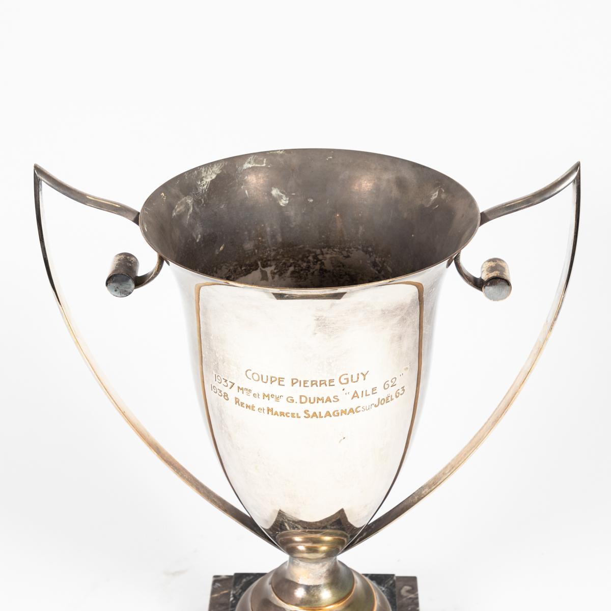 French modernist silver-plate trophy mounted on a stepped taupe and black marble base, featuring winged scroll-tipped handles. The piece was originally awarded to winners of the 