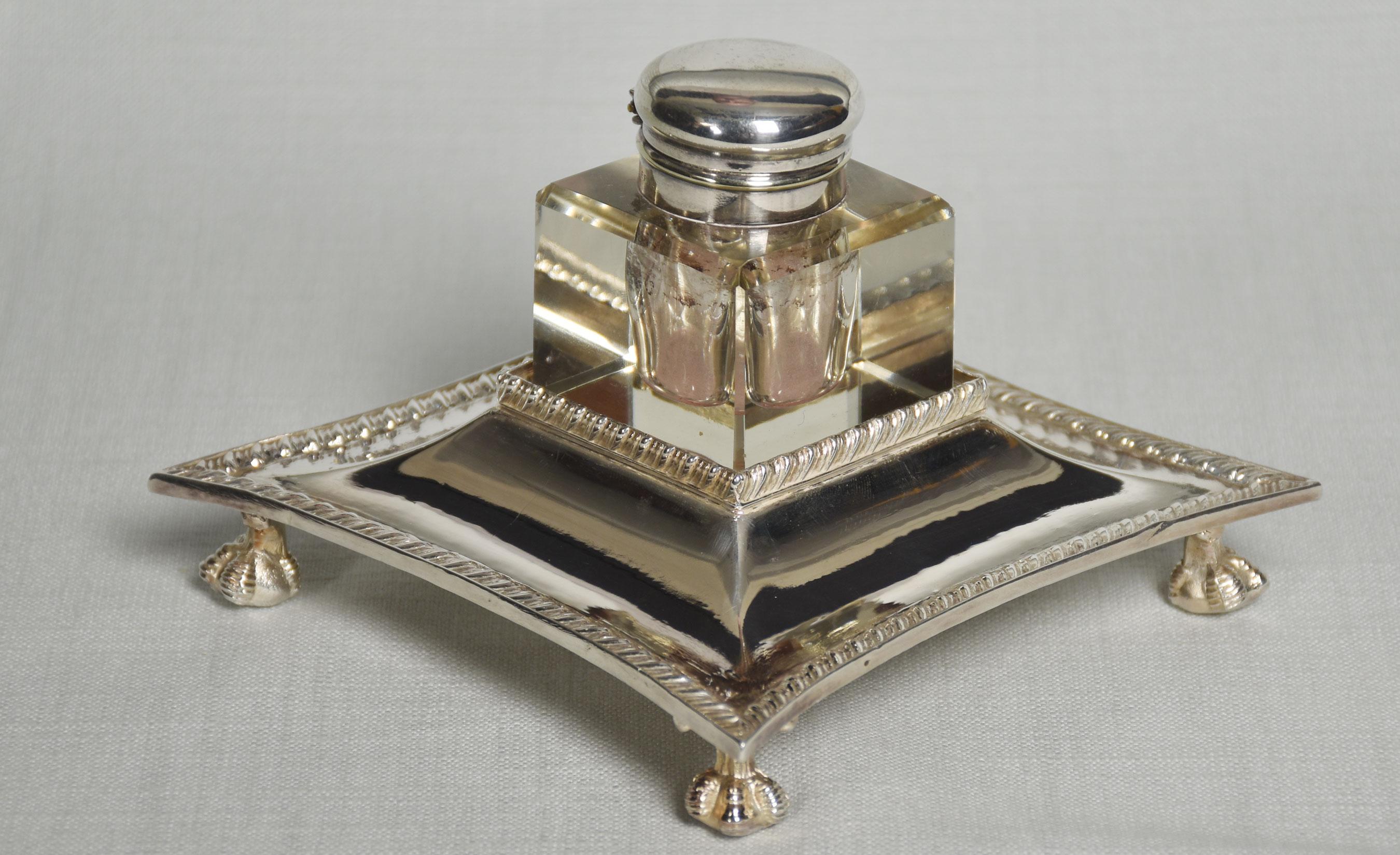 A silver-plated and clear glass ink well and stand, shaped square plated Stand with gadroon borders raised on four claw and ball feet supporting square glass well with plated hinged cover, stamped Walker & Hall, Sheffield.
Dimensions
Height 4