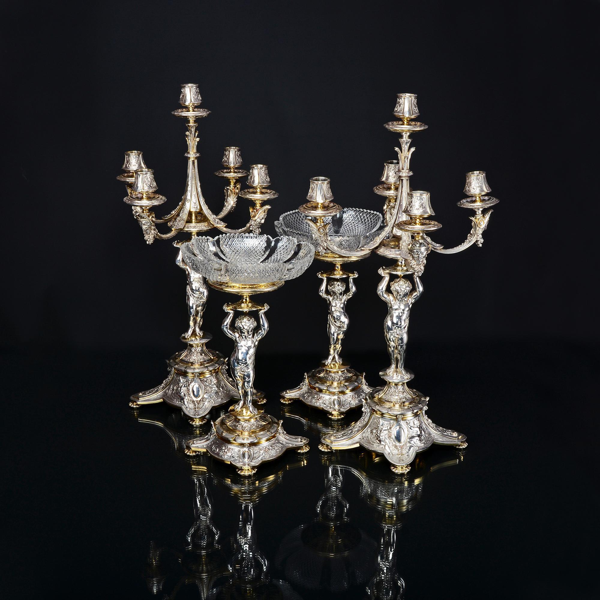 Fine quality and highly decorative suite of silver-plated and partial gilt candelabra and comports. All four pieces have central cast and finely detailed puti or cherubs, each upholding either the branches of the candelabra or the compressed