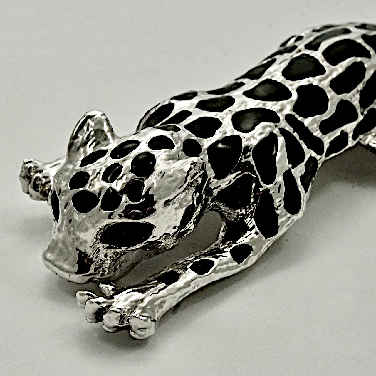 Broche élégante en métal argenté représentant un chat léopard avec des yeux en strass noir et une queue mobile. Il s'agit d'une grande broche mesurant 13 cm de long pour une largeur maximale de 3,6 cm. La broche est en très bon état.

Cette