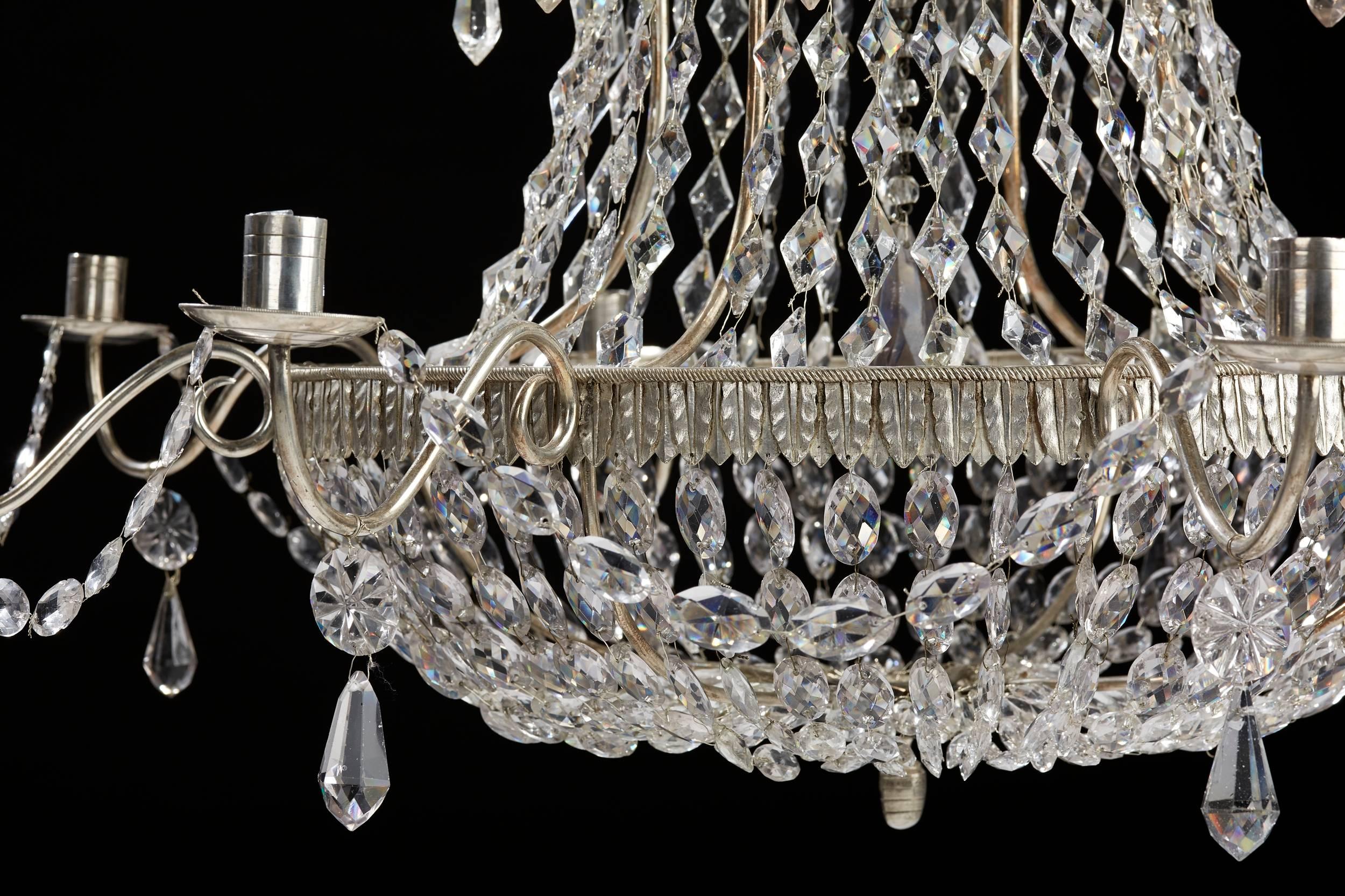 A Russian silver plated bronze and cut glass sixteen-light chandelier, 19th century.
The top hung with facetted drops above a baluster cut glass stem within long chains of faceted drops hanging from the top. Middle center corona issuing eight