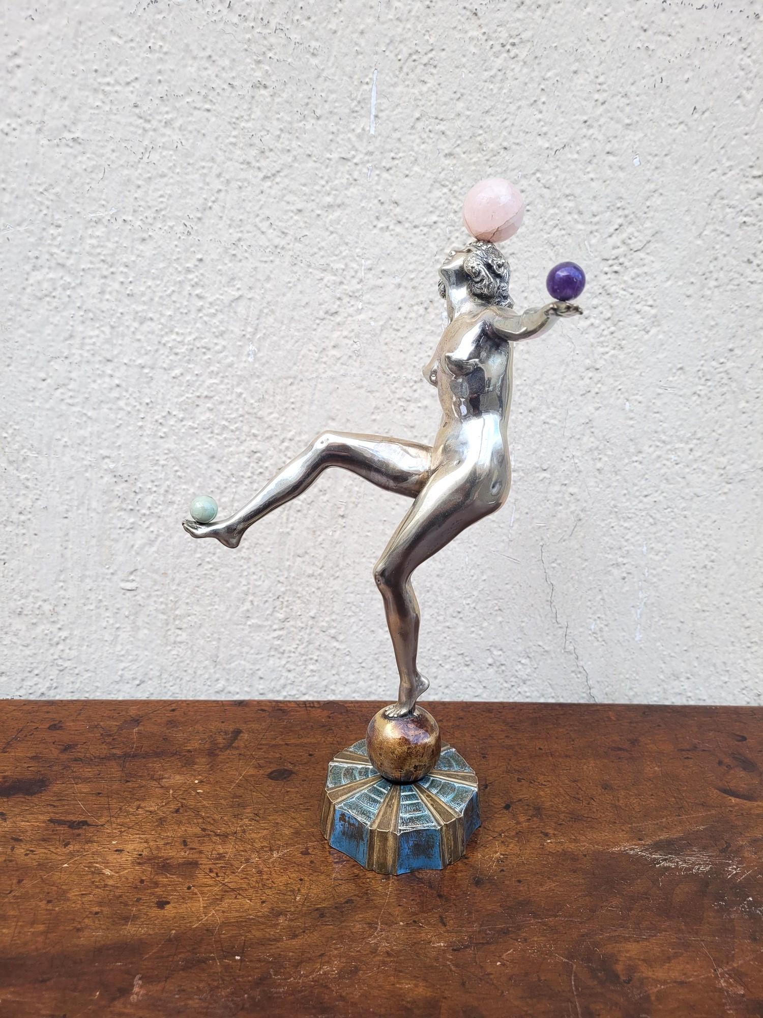 Grande scultura in bronzo argentato e patinato che rappresenta una ballerina in equilibrio su una palla e che si destreggia con delle palline.

Queste sfere sono realizzate con pietre dure: ametista, quarzo rosa e pietra verde.

Bronzo tipico del