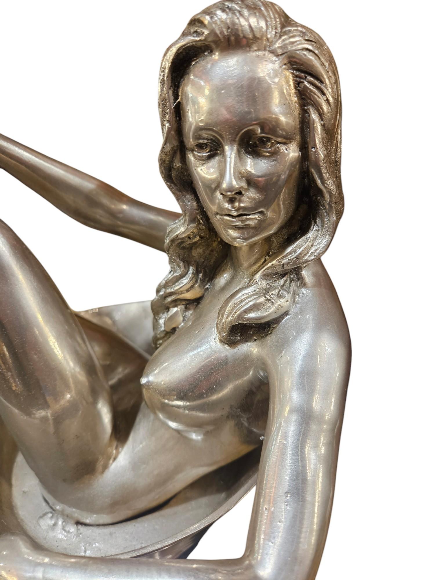 Una scultura placcata in argento raffigurante un nudo femminile erotico seduto in una coppa di champagne
Firmato sulla base
