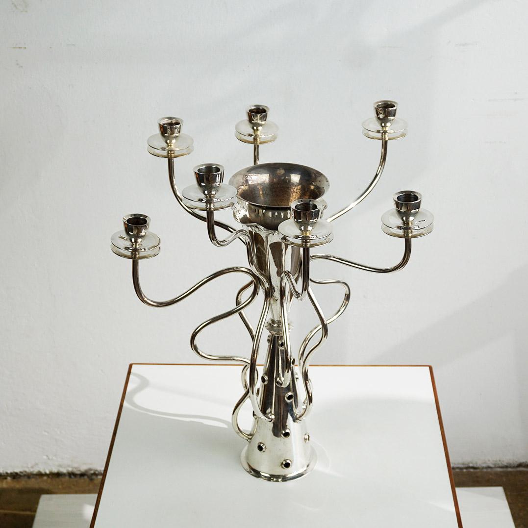 Questo portacandele a sette bracci è stato disegnato da Borek Sipek nel 1988 e prodotto da Driade. È realizzato in metallo argentato con il timbro dell'azienda Driade sul lato inferiore. Il corpo conico è circondato da sette bracci avvolgenti