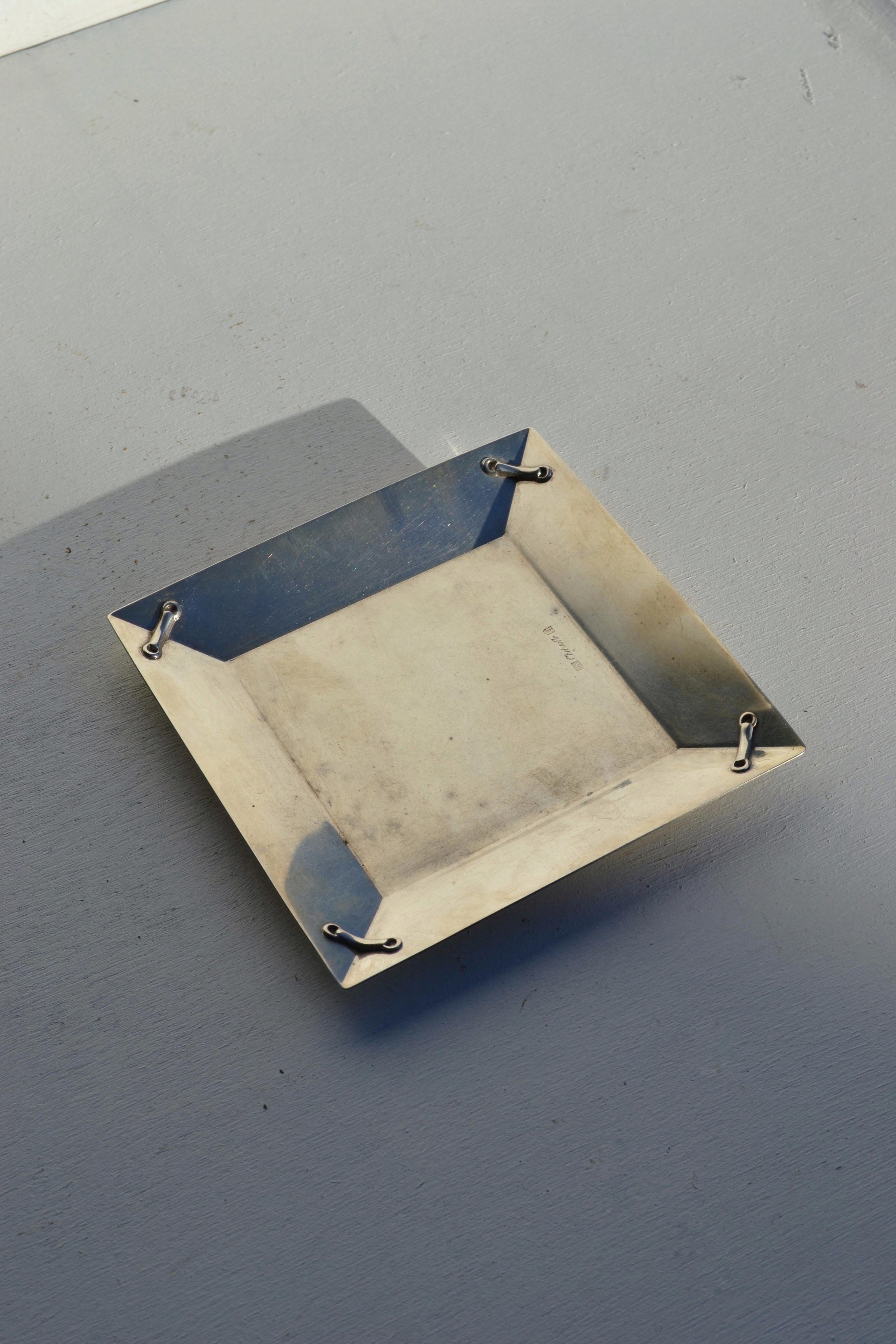 Eleganza del cestino quadrato placcato in argento di Christofle.
Il suo design geometrico e minimalista è impreziosito da quattro piccoli dettagli in metallo fissati ad ogni angolo, che mettono in mostra la raffinata abilità artigianale del rinomato