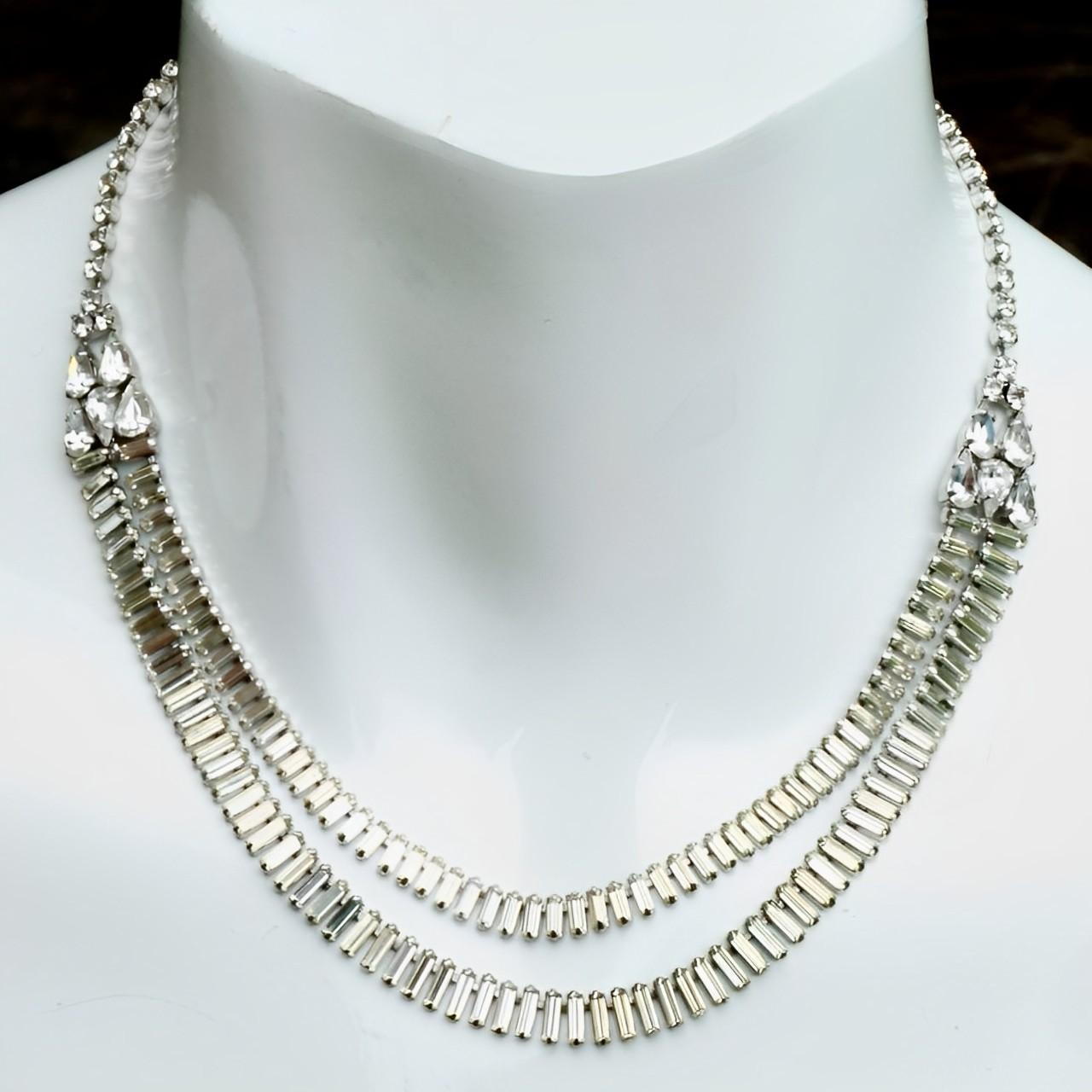 Beautiful silver plated necklace set with a double strand of baguette rhinestones. The strands are joined together by a cluster of marquise rhinestones and a single strand of round rhinestones. The necklace fastens with an adjustable hook. There is
