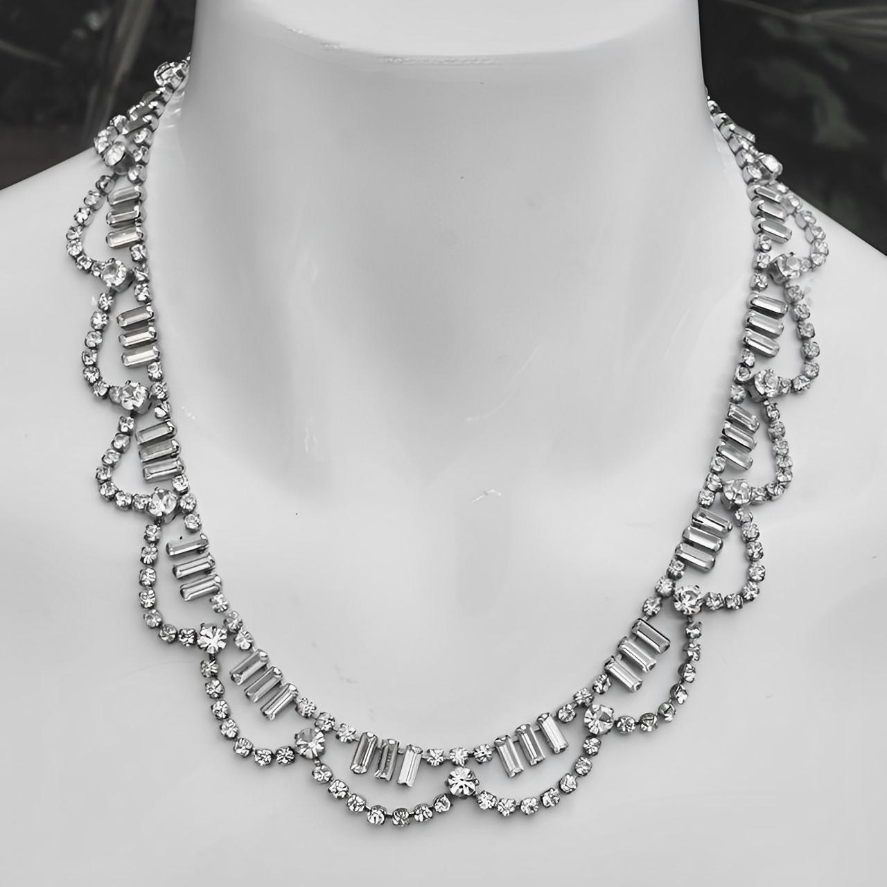 Bellissima collana a festone placcata in argento, con strass rotondi e baguette. L'estremità della collana è stata sostituita da una catena per renderla più lunga.

Misura 45,7 cm di lunghezza.

Questa deliziosa collana di strass ha un design