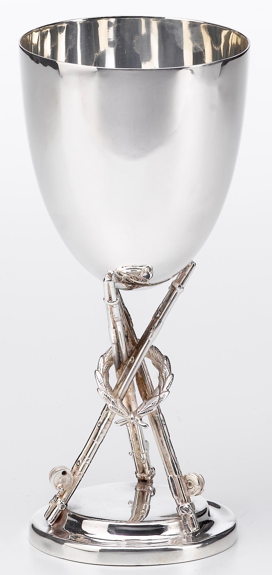 This silver trophy was designed to celebrate the winner of an angling competition. Three fishing rods with large reels intersect over one another, forming a three-pronged base for the trophy. Looped onto the rods is a wreath, signifying victory for