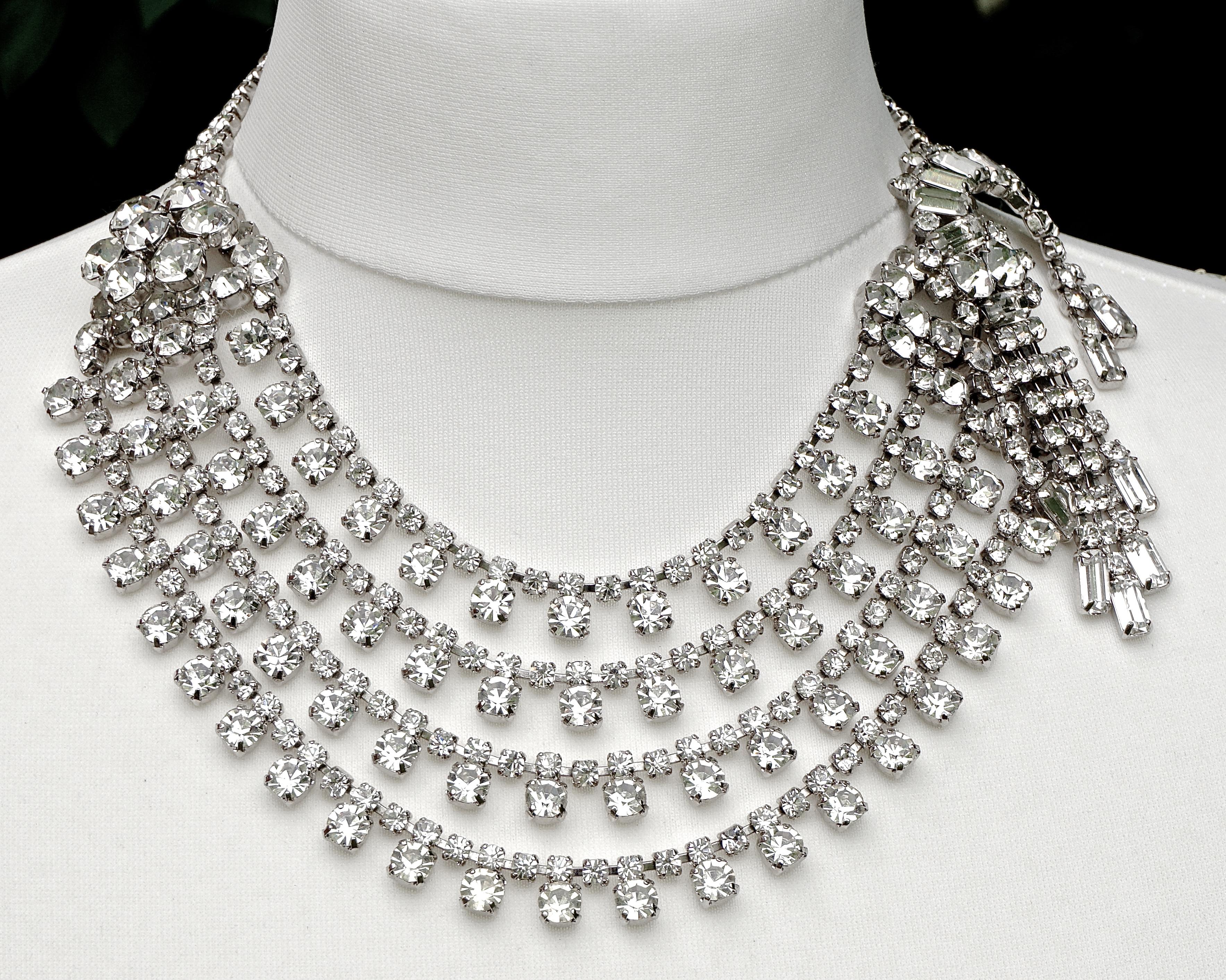 
Fabulous silver plated four strand rhinestone collar necklace. The necklace has a cluster of five large rhinestones to one side, and the other side features a wonderful tremblant design with round and baguette rhinestones. The shortest length is