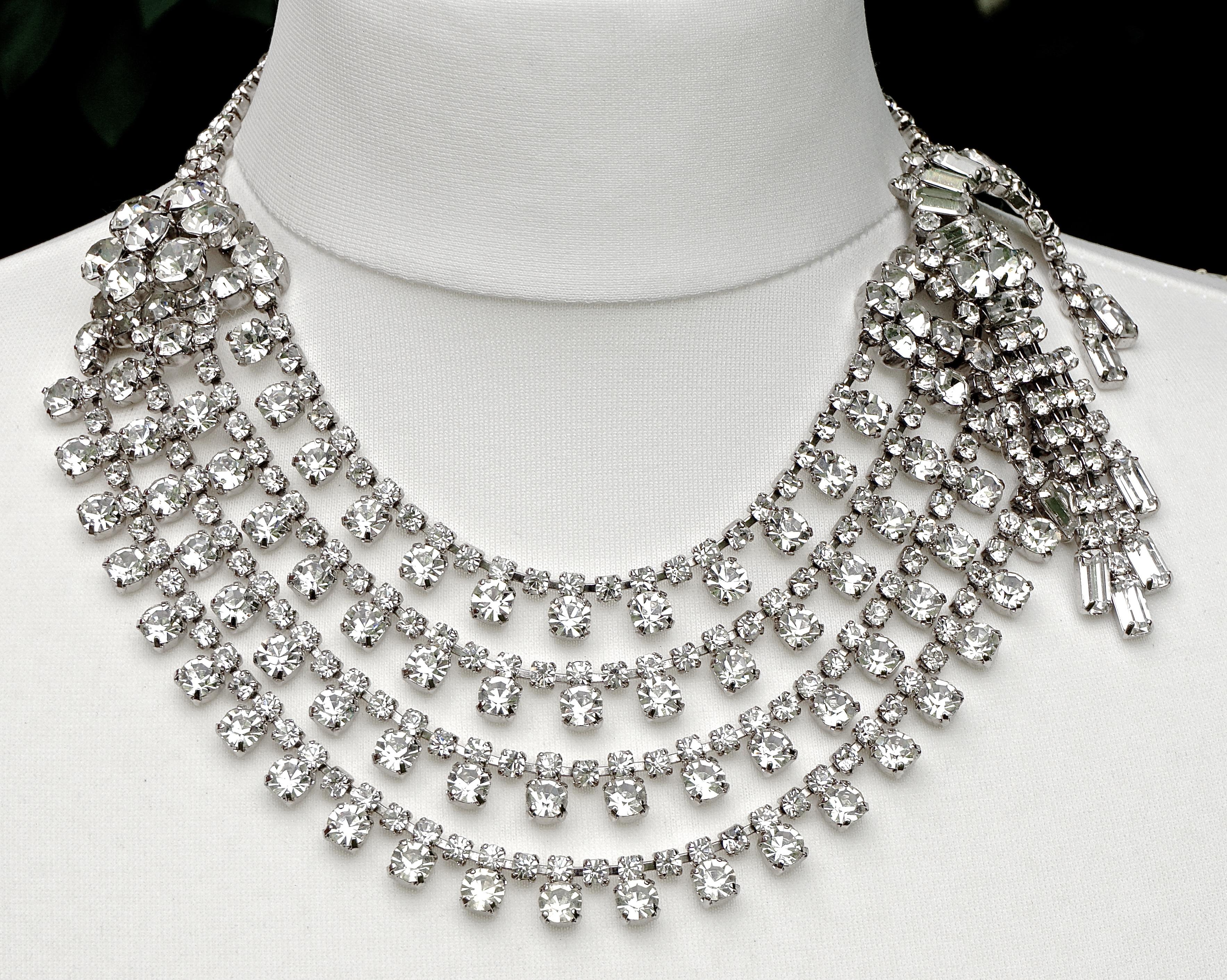 
Favolosa collana a quattro fili con strass placcata in argento. La collana presenta un gruppo di cinque grandi strass su un lato, mentre l'altro lato è caratterizzato da un meraviglioso disegno tremblant con strass rotondi e baguette. La lunghezza