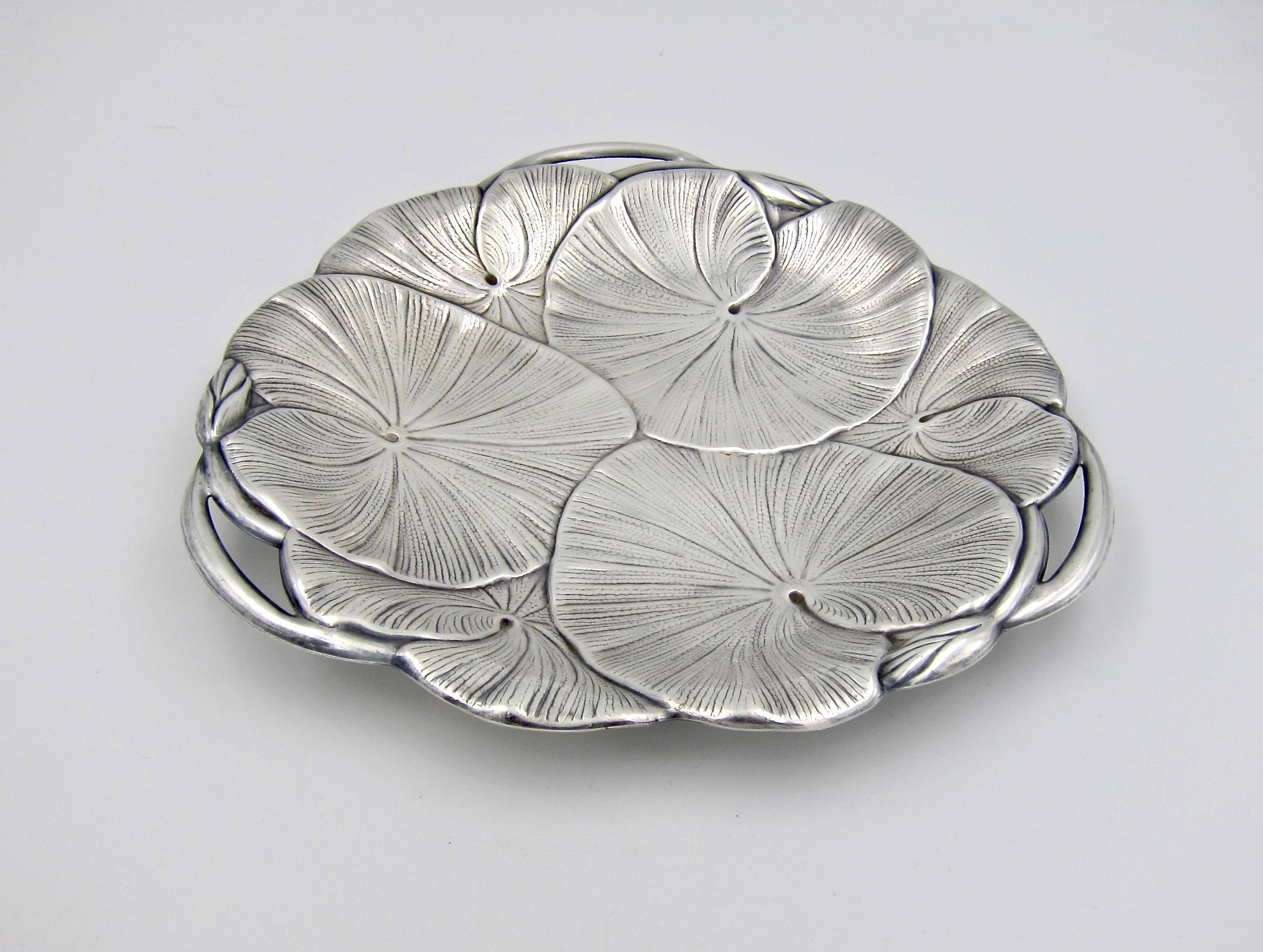 An American Art Nouveau tray from Wilcox International Silver Company of Meriden, Connecticut, dating circa 1930s. The design features overlapping lily pad leaves with three buds and three open handles around the outer rim. The vintage silver-plated