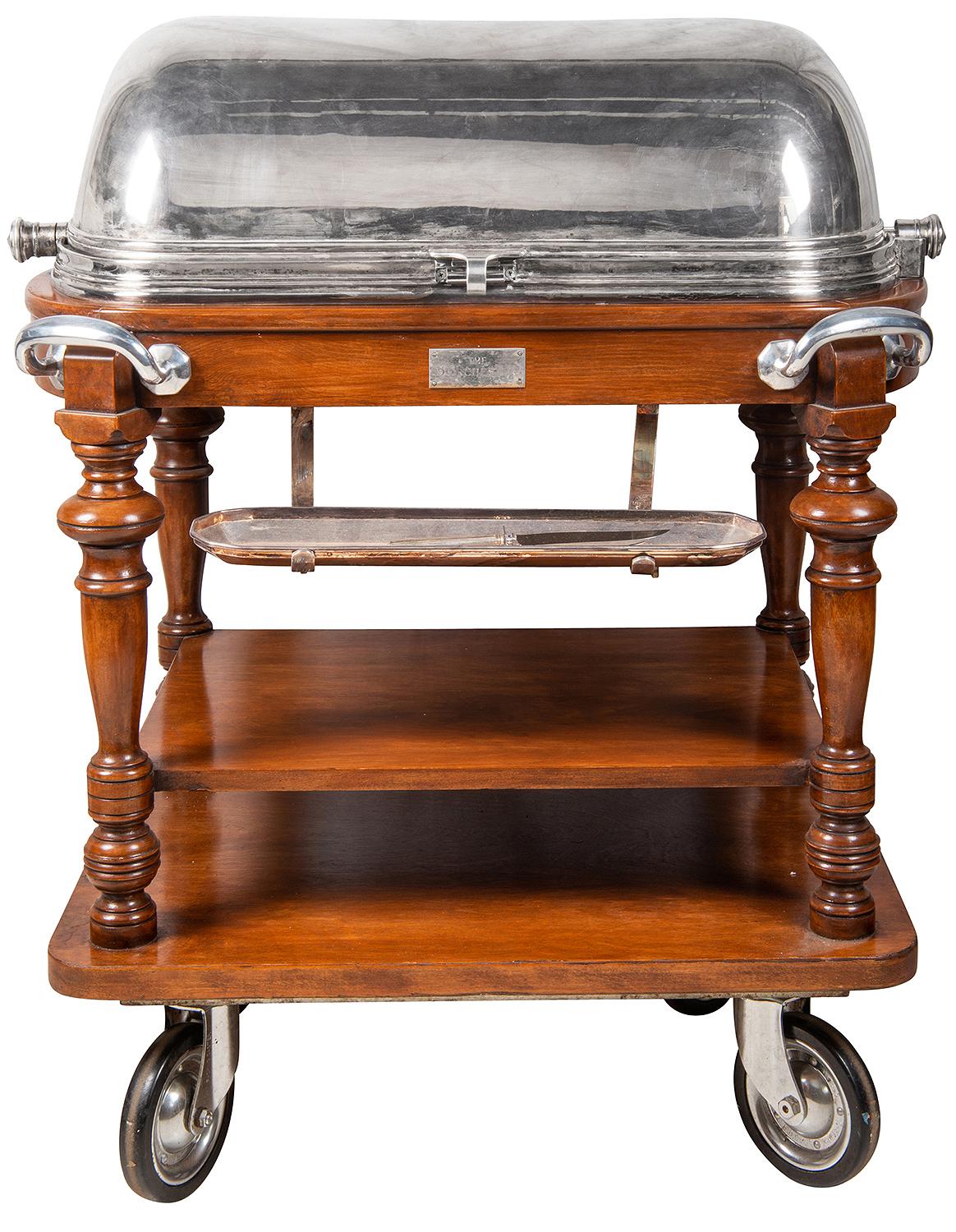 A very good quality early 20th century silver plated and mahogany carving trolley, having a domed, hinged lid opening to reveal the carving surface, lidded containers, carving implements, shelves below, turned legs, silver plated handles and raised