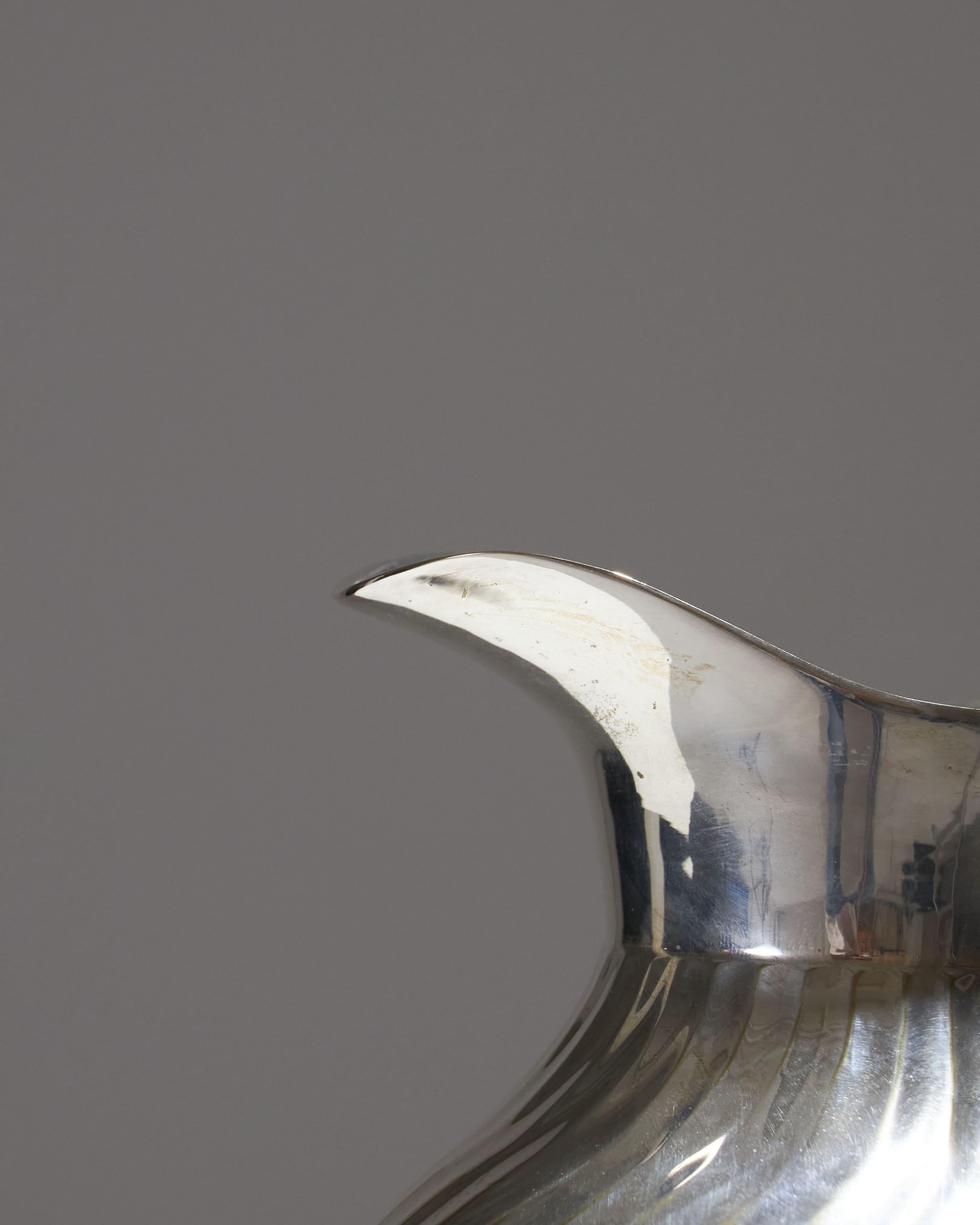 Silver-plated metal pitcher with an elegant raised swirl pattern. The handle is ornamented, and the base features a two-tiered design. This pitcher combines aesthetics and functionality, bringing a touch of timeless luxury to your table. Perfect for