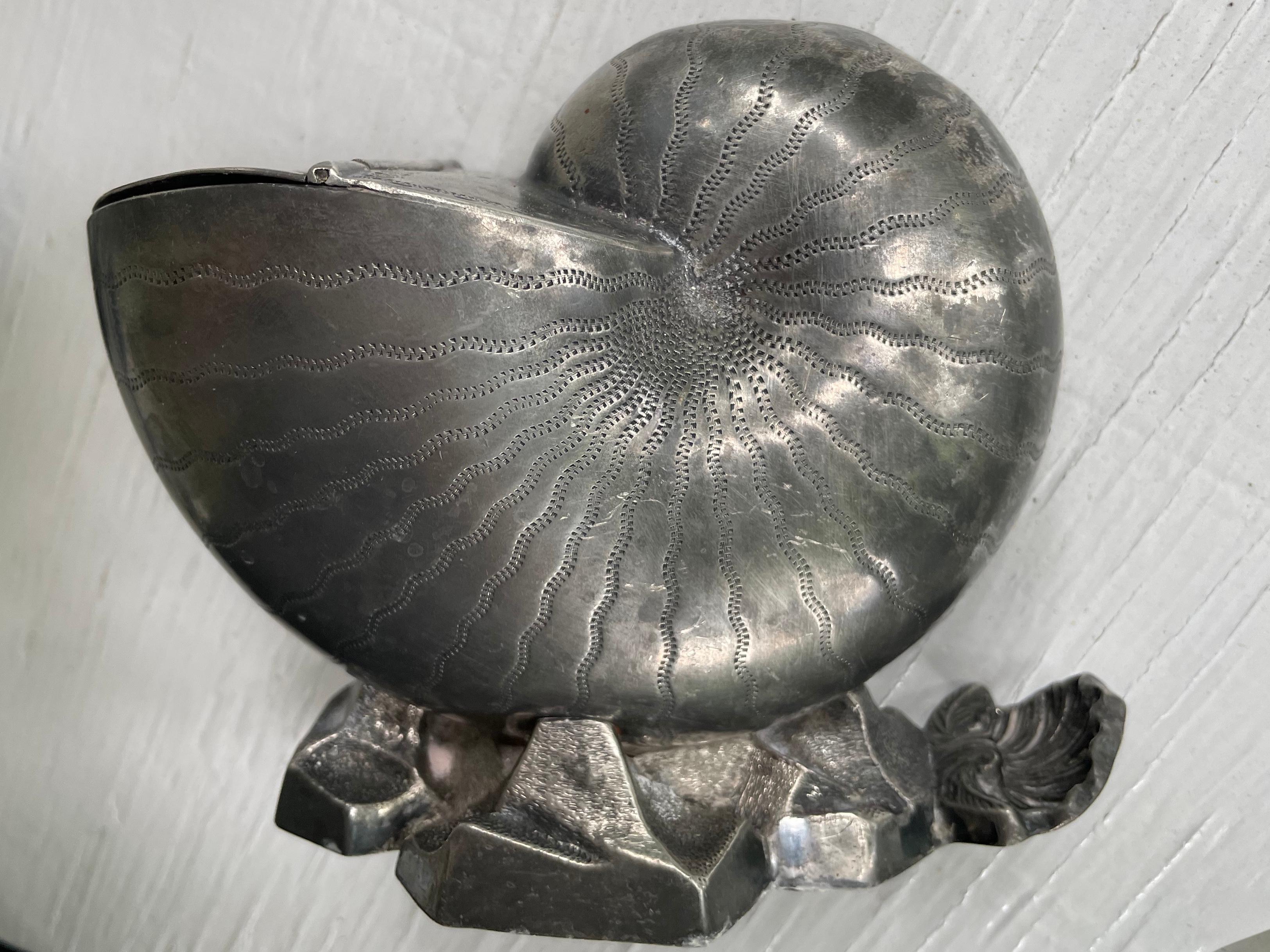 Silver plated nautilus sculpture. Antique English silver plated spoon warmer in the shape of life size nautilus shell with hand hammered decorations to shell, and lid resting on a rock form base with shell handle. England, Circa 1880. 
Dimensions: