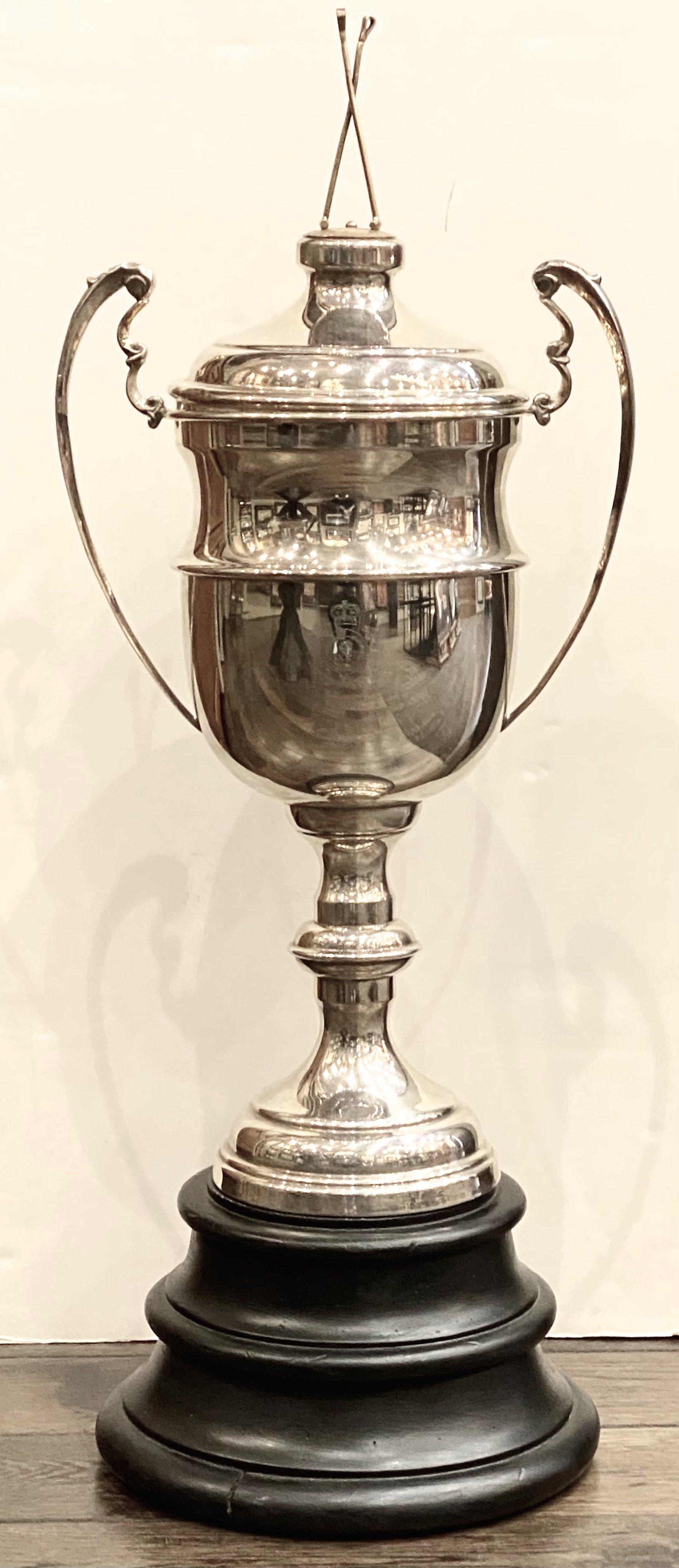 Offered is a vintage polo trophy, dating to 1910. This large and decorative trophy is plated in silver and stands on a wooden base, which is removable. It is completed with a large lid with two interlocked polo sticks. The trophy also has large,