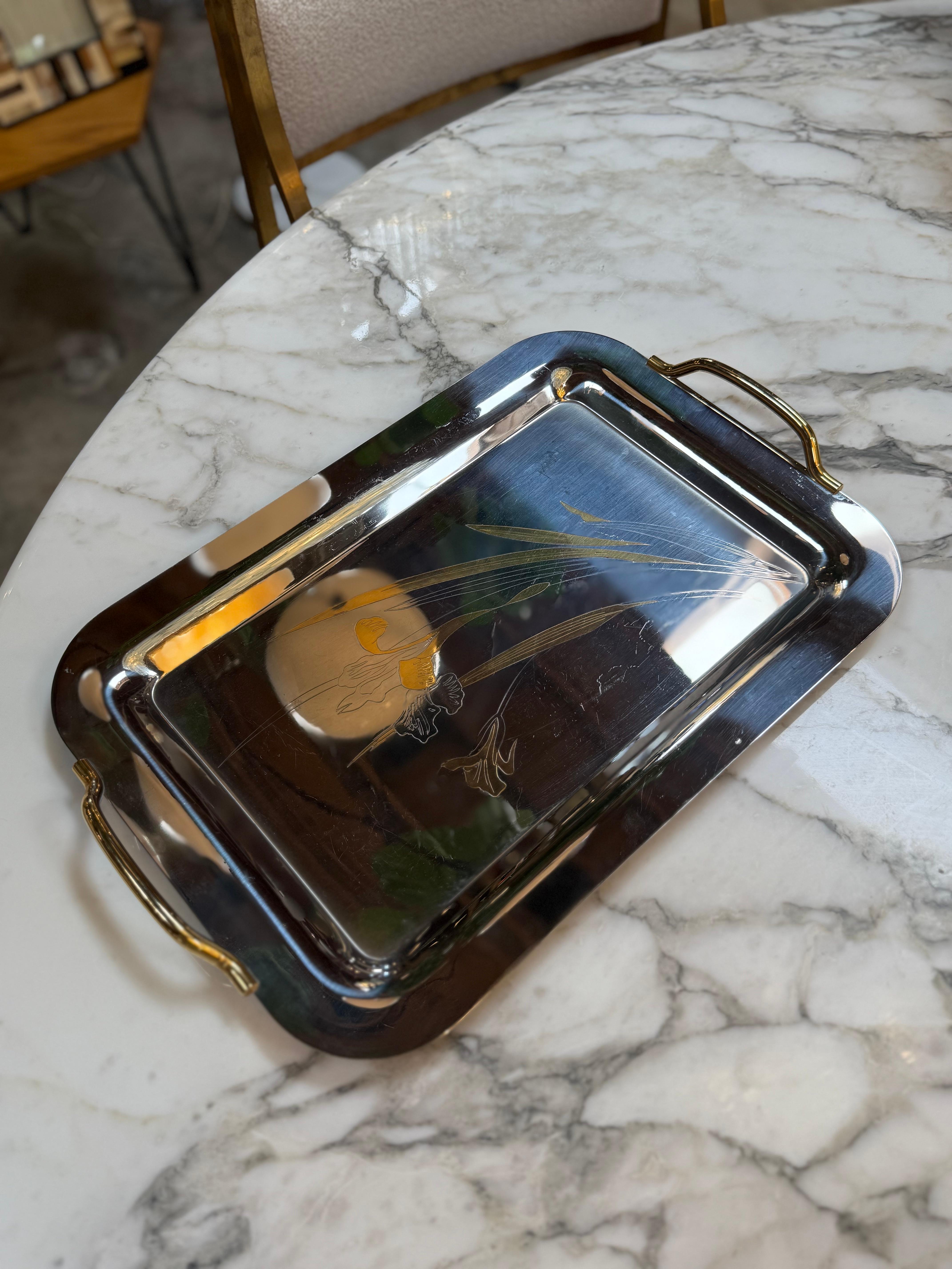 Elegant vintage rectangular metal tray featuring a gold-tone floral etching with graceful blossoms and leaves on a polished silver-tone surface. The tray includes curved gold handles and a raised rim, combining decorative artistry with functional