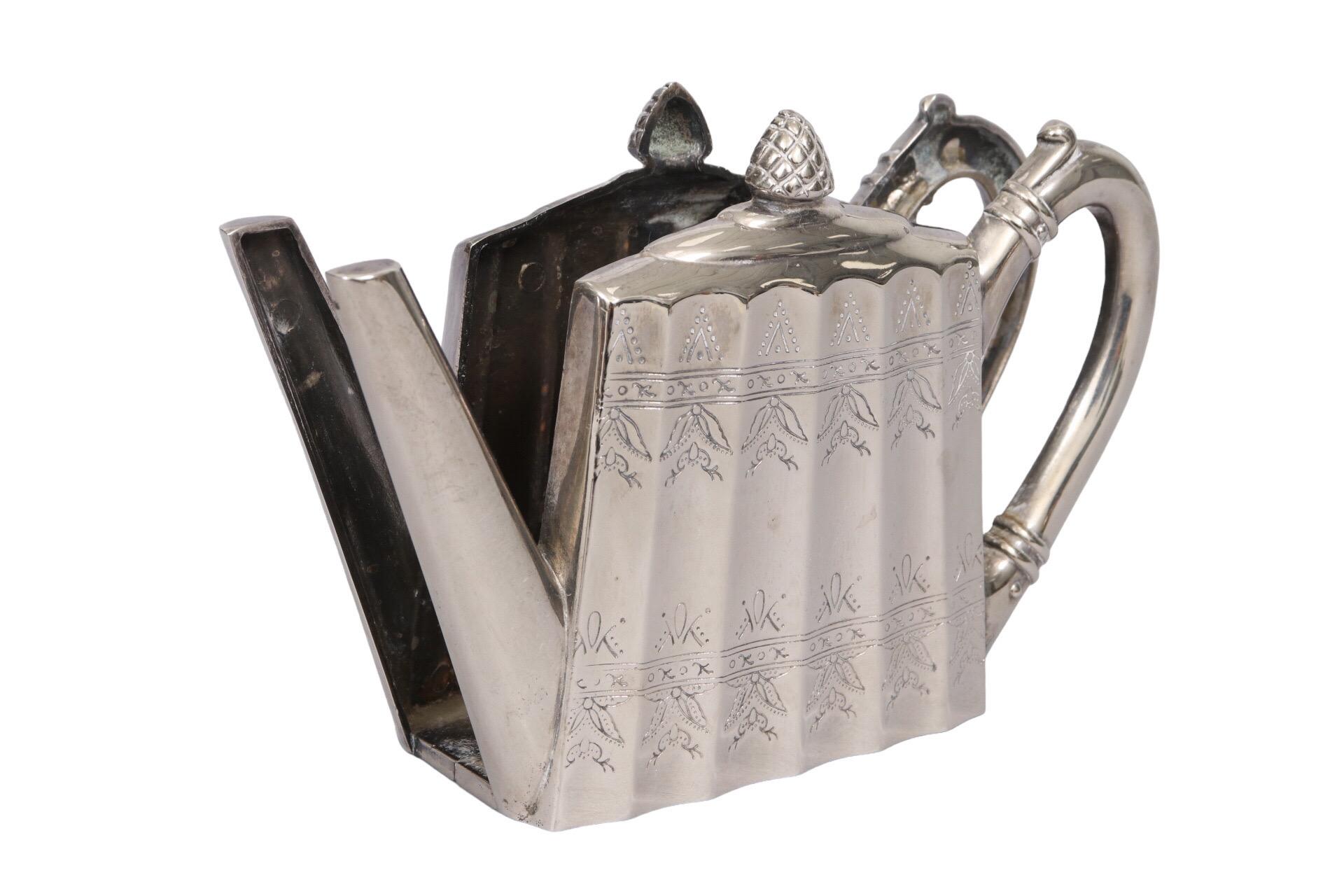 An engraved silver-plated napkin holder made by Godinger. Shaped like a teapot with a scalloped body and repeating floral motif. Marked Godinger Silver 1998 underneath.
