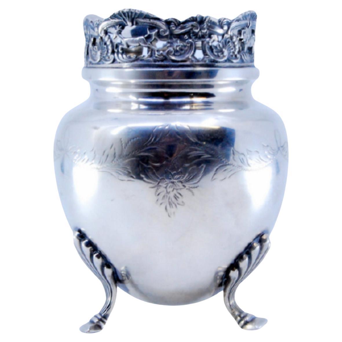 Silver pot resting on three support feet and rim with cut-out grate
