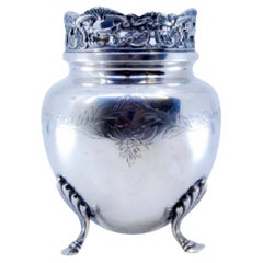 Silver pot resting on three support feet and rim with cut-out grate